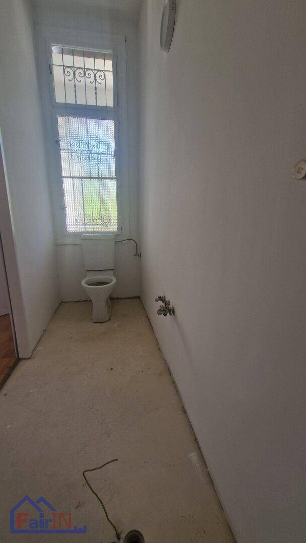 Schmaler Toilettenraum mit Fenster, Sicherheitsgitter und einfachen Sanitäranschlüssen.