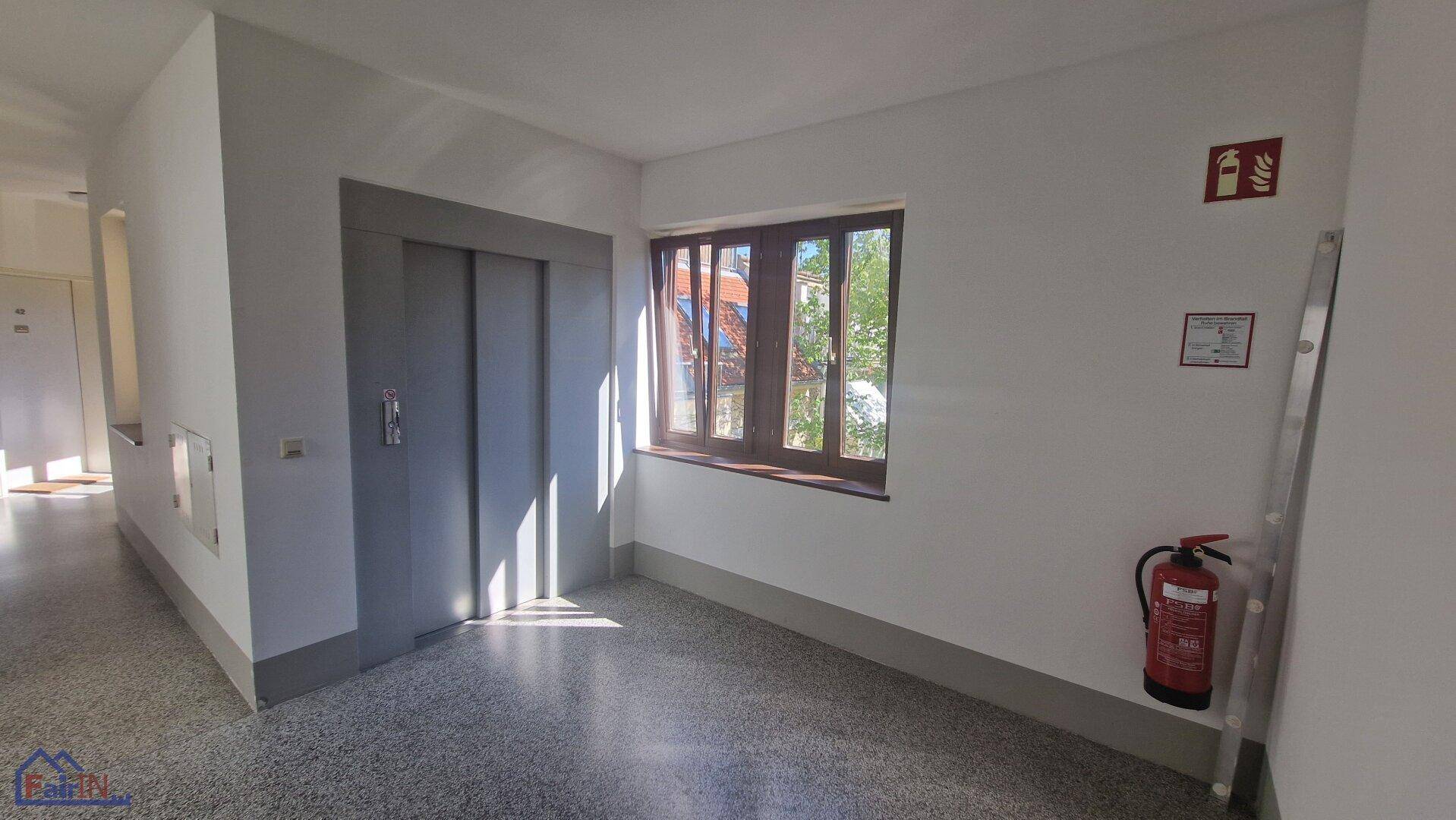 Heller Flur mit Aufzug, Fenster und Terrazzoboden im Gemeinschaftsbereich.