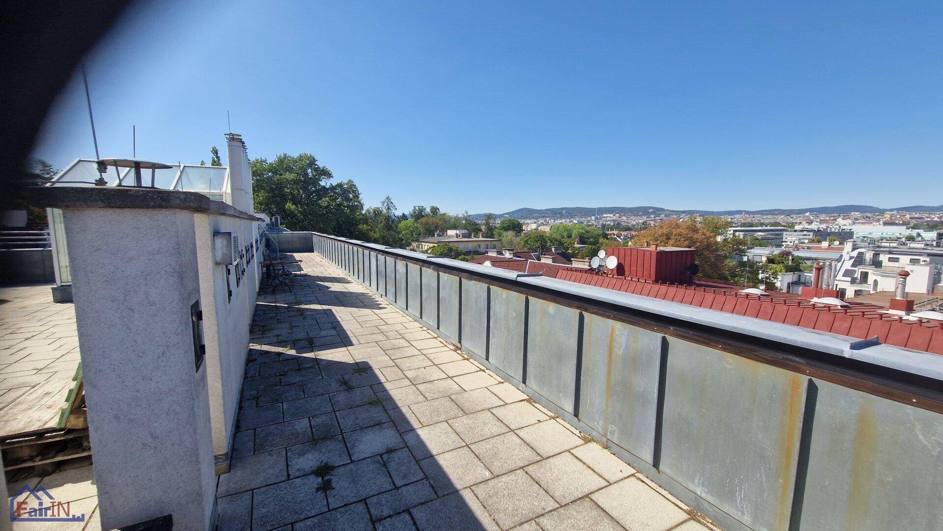 Lange Dachterrasse mit Fliesenboden, Metallgeländer und weitem Stadtblick.