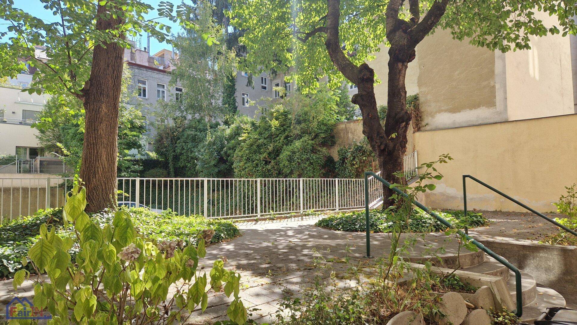 Grüner Innenhof mit alten Bäumen und einem weißen Zaun, der zum Entspannen einlädt.