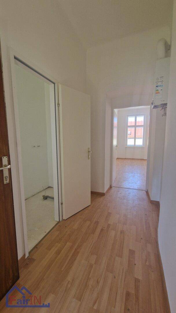 Heller Flur mit Holzboden und Blick in angrenzende, leere Räume.
