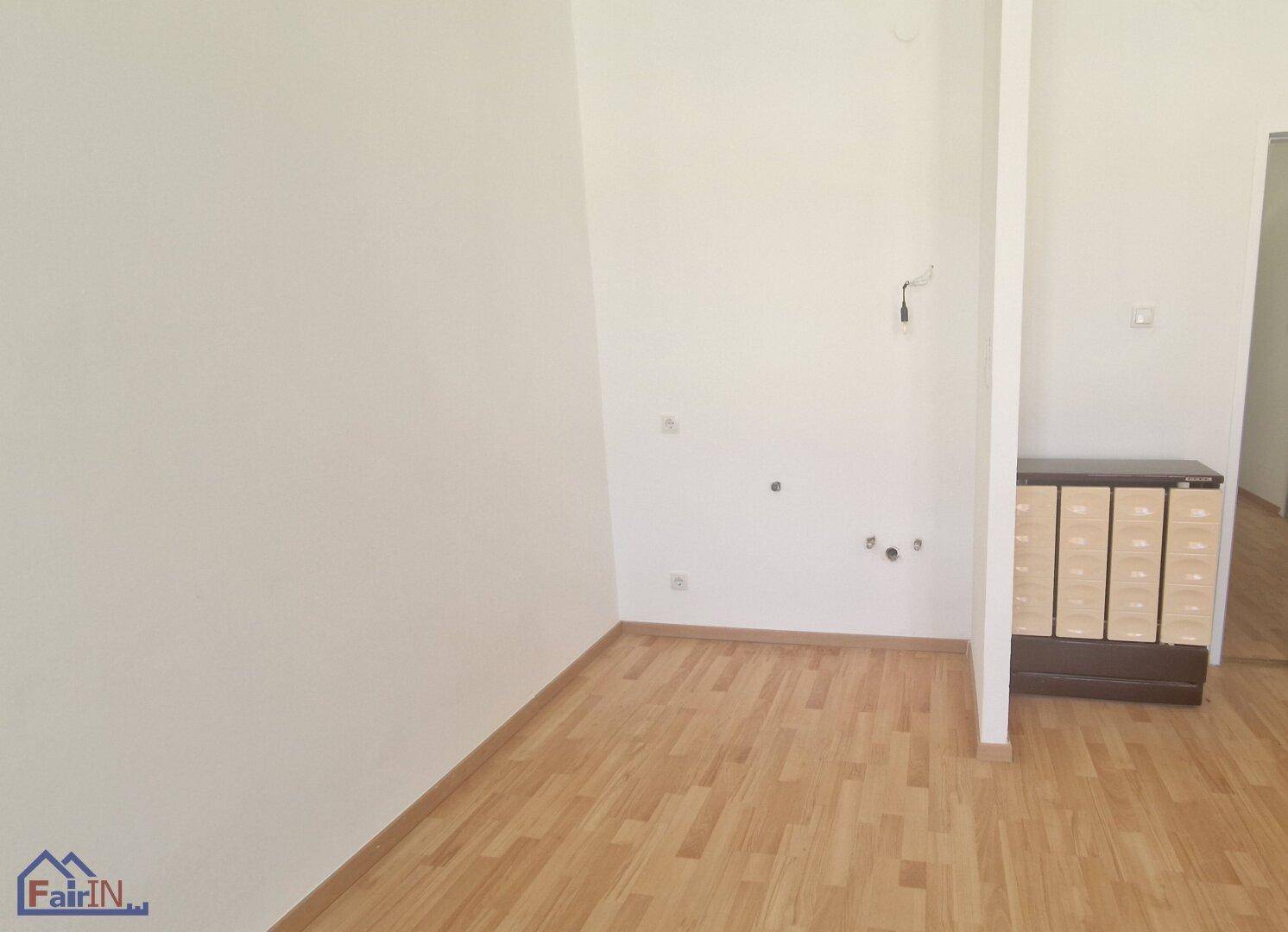 Leerer Raum mit Holzboden und Anschlüssen an der Wand, möglicherweise für eine Küche.