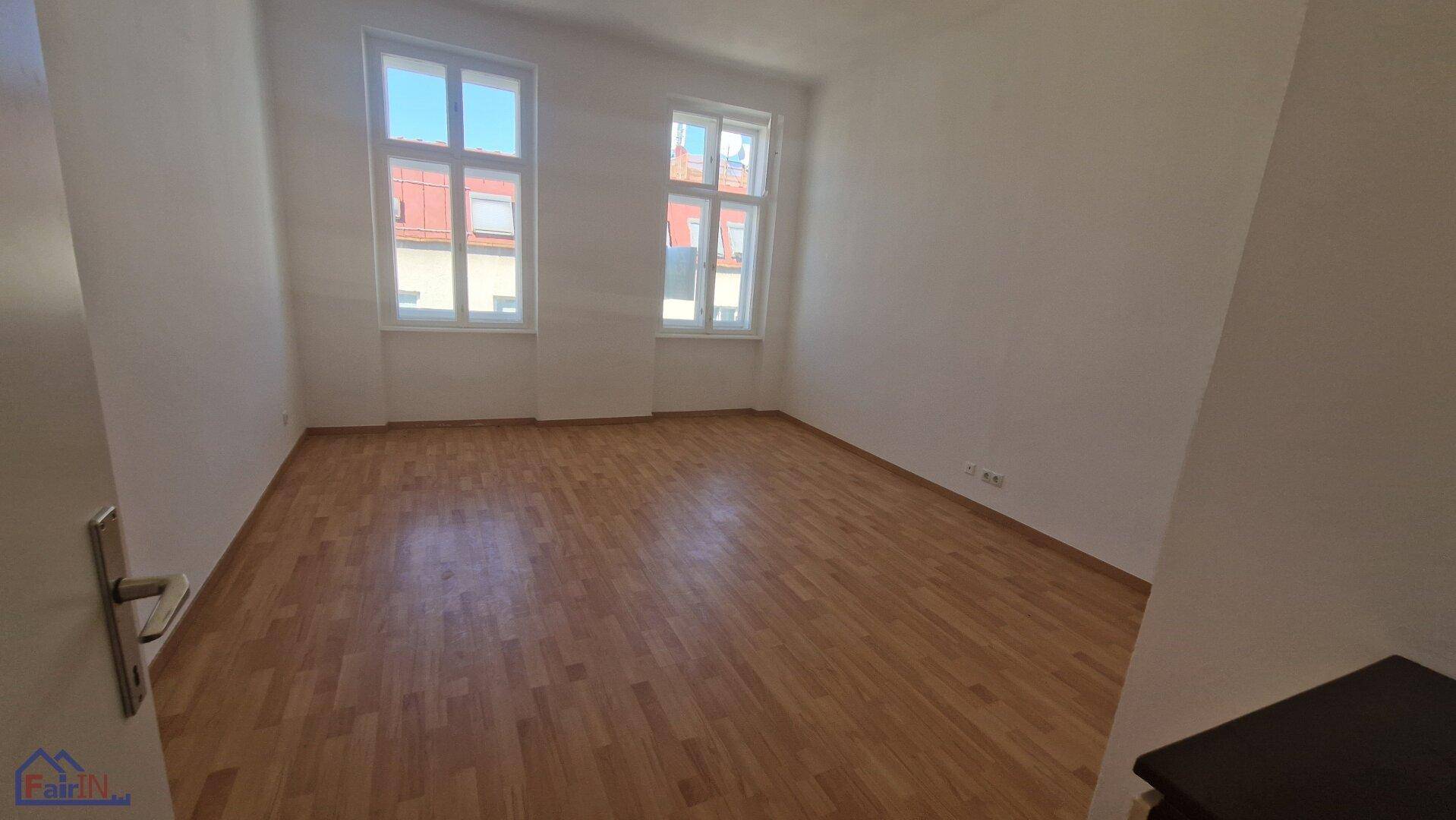 Geräumiger, heller Raum mit Holzboden und zwei großen Fenstern, bereit zur Einrichtung.