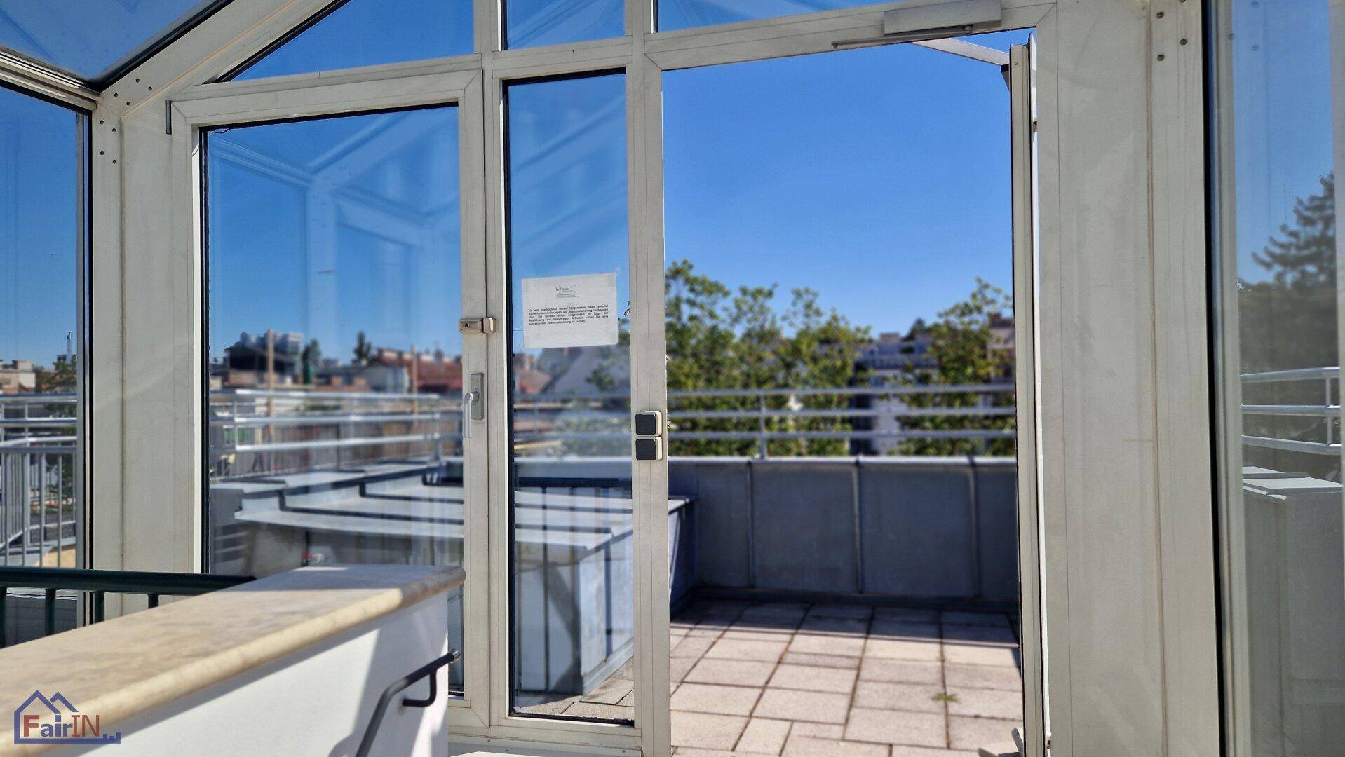 Verglaster Zugang zu einer sonnigen Dachterrasse mit Stadtblick.