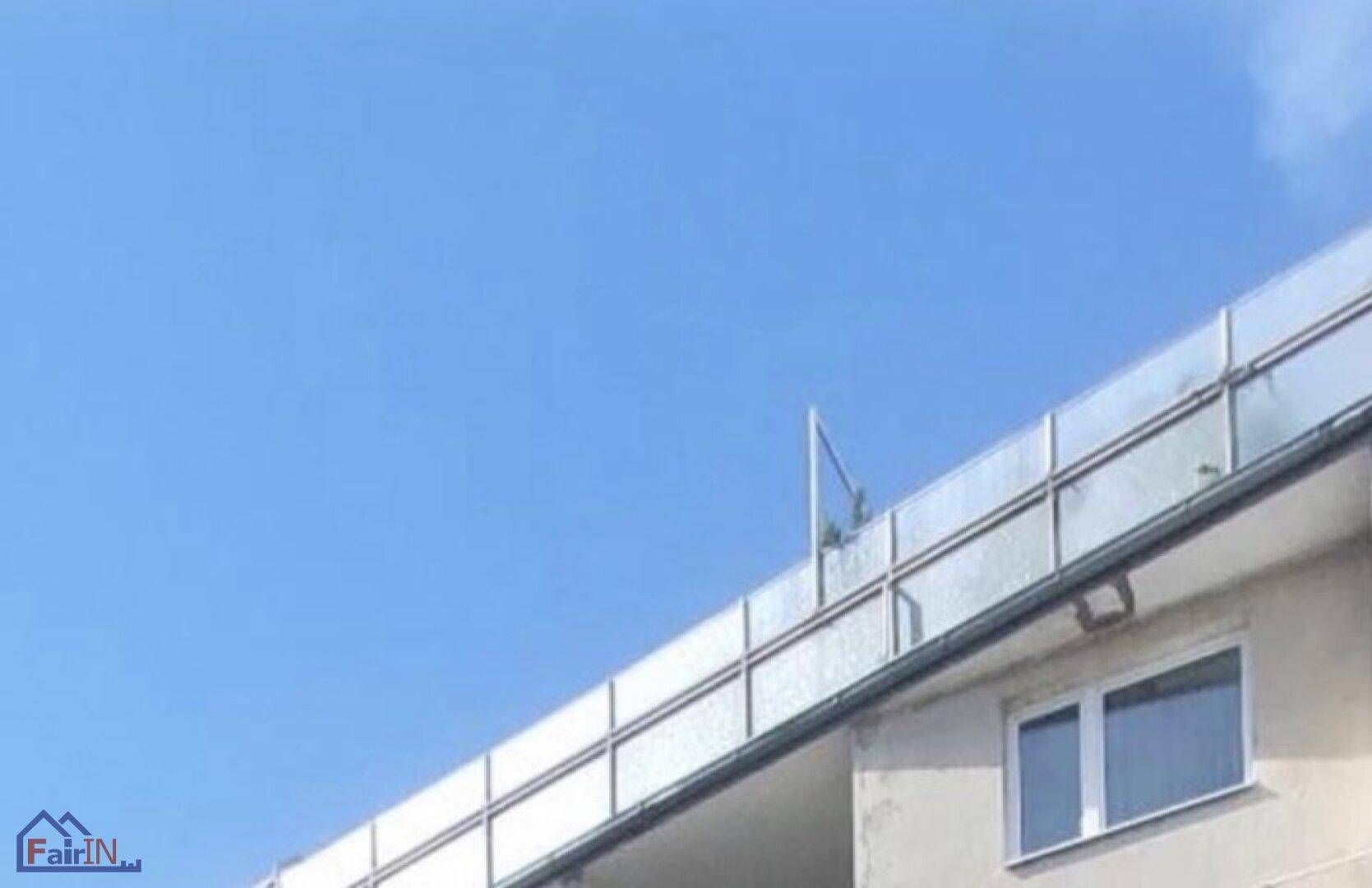 Heller Balkon mit modernem Glasgeländer und weitem Blick in den blauen Himmel.