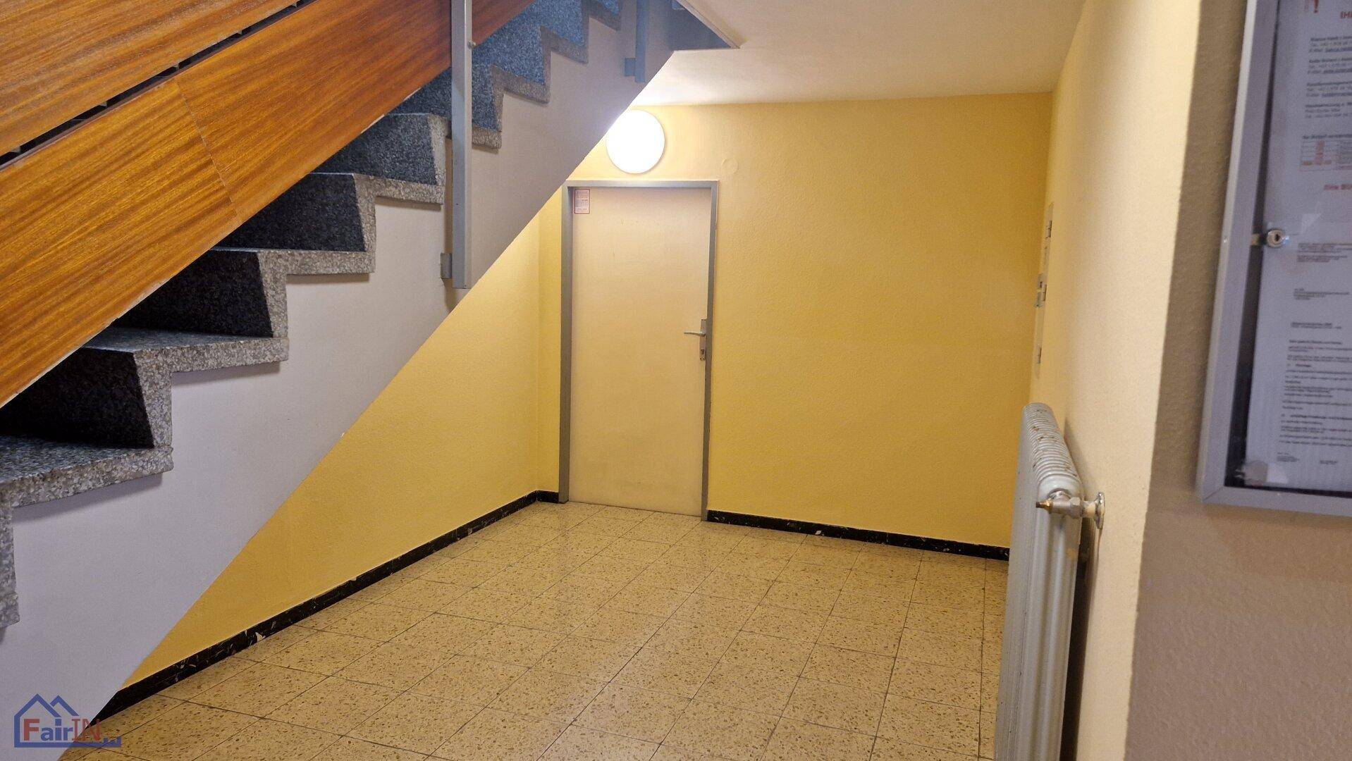 Treppenhaus mit Granitstufen und Holzgeländer, gelben Wänden und Fliesenboden.