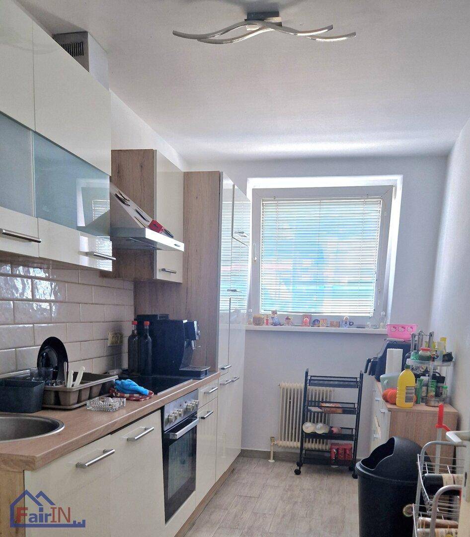 Moderne Küche mit weißen Hochglanzschränken, Holztheke und einem Fenster mit Jalousien.