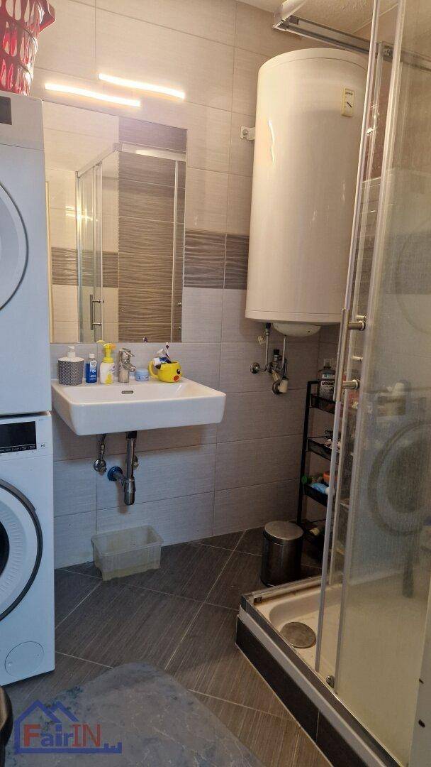 Badezimmer mit Waschbecken, Duschkabine und einem Warmwasserboiler an der Wand.