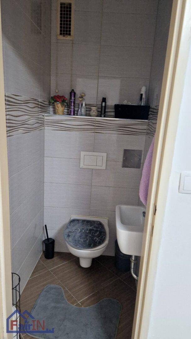 Separates WC mit Wandtoilette, kleinem Waschbecken und modernen Fliesen.