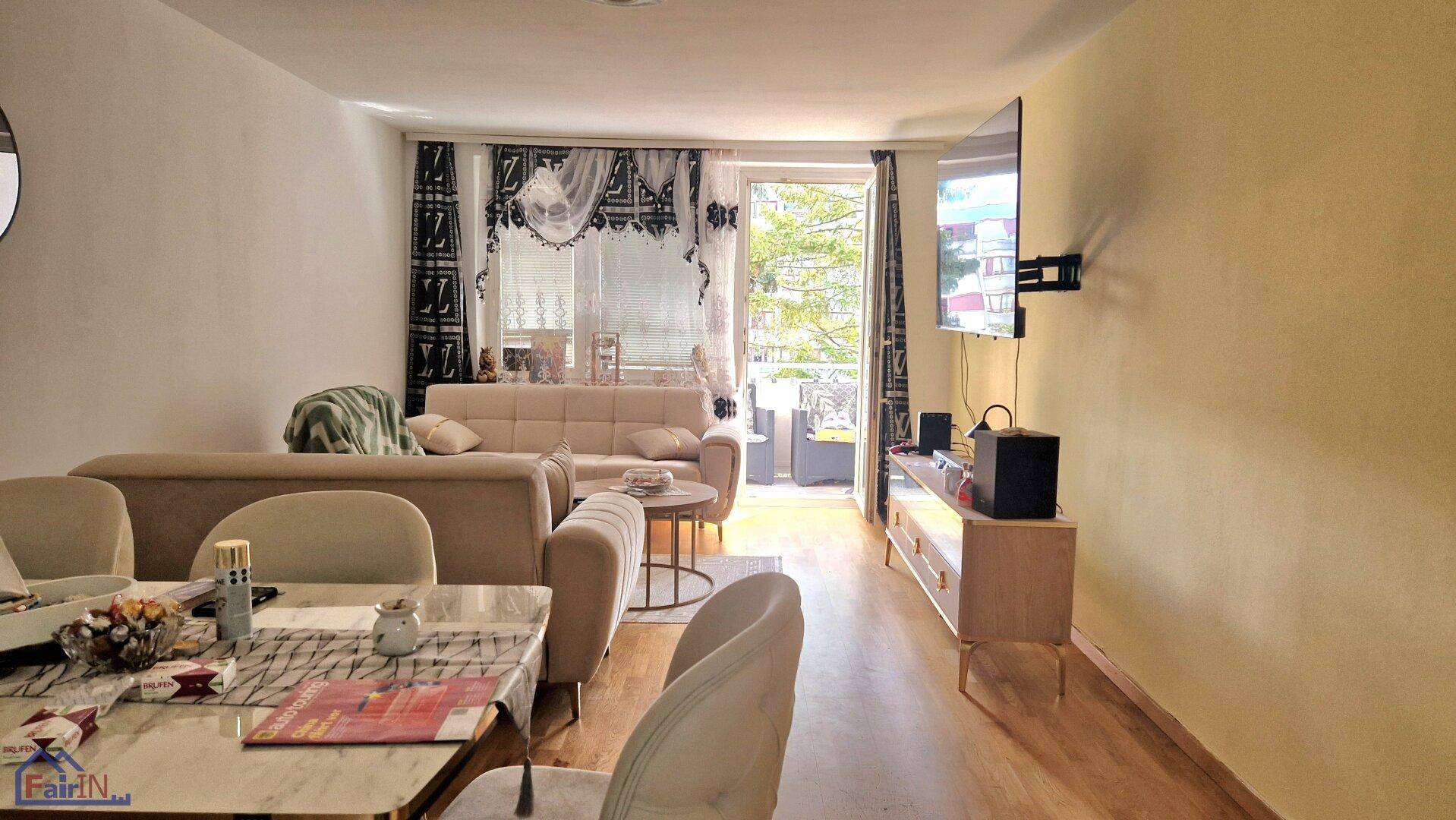 Geräumiger Wohn- und Essbereich mit Zugang zu einem Balkon und einem Fernseher an der Wand.