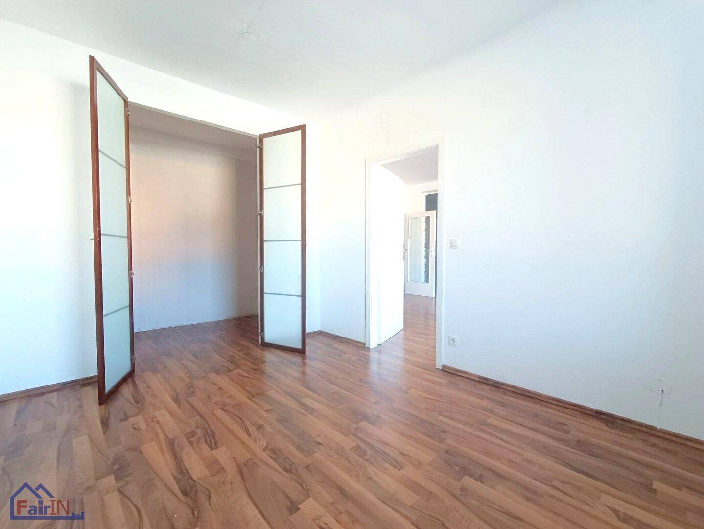 Heller Wohnraum mit Laminatboden und eleganten Glastüren zu einem weiteren Zimmer.