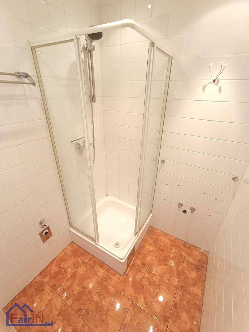 Badezimmer mit Eckduschkabine, weißen Wandfliesen und Terrakotta-Fliesenboden.