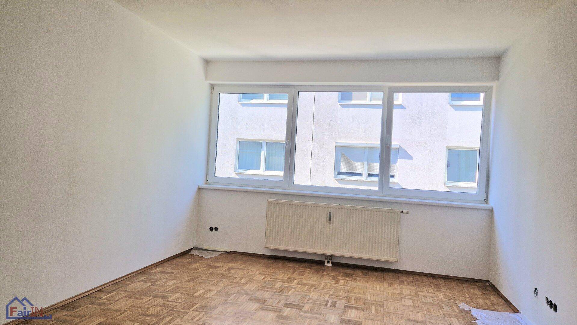 Helles, leeres Zimmer mit Parkettboden, großem Fenster und Heizkörper, bereit zur individuellen Gestaltung.