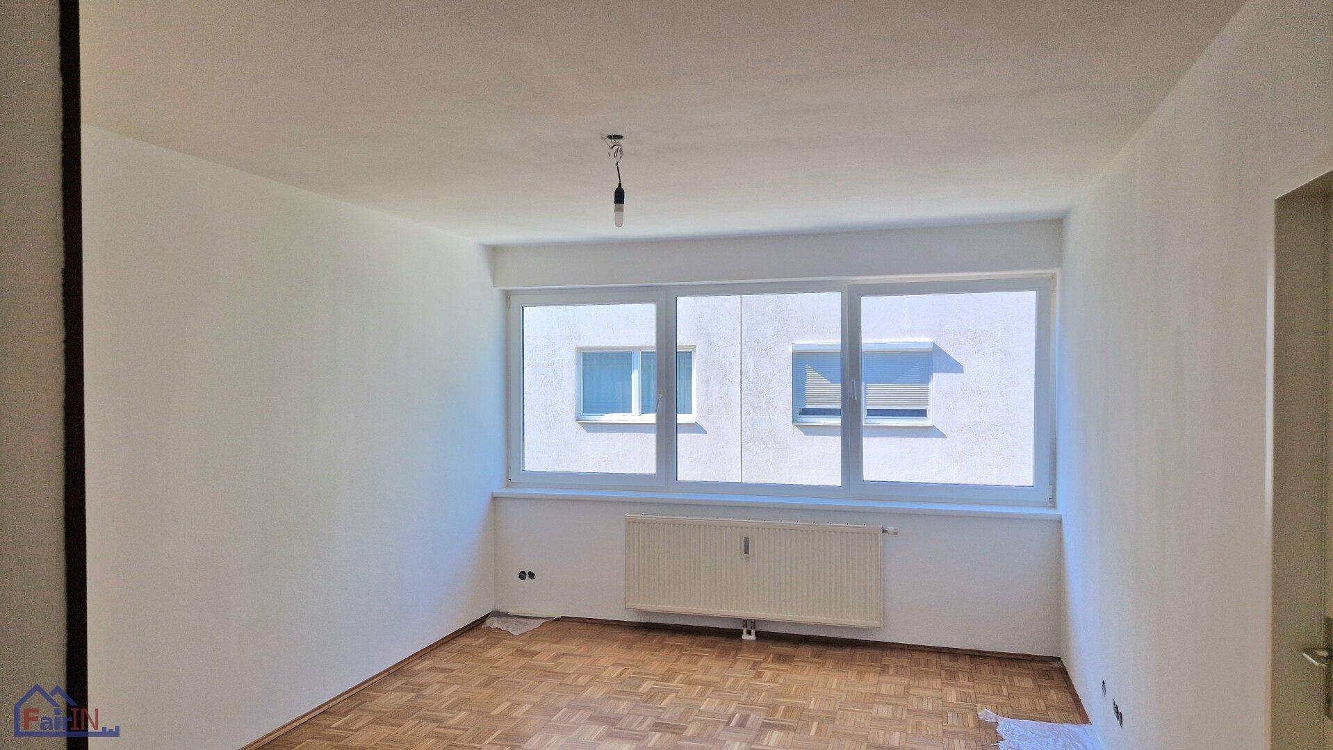Lichtdurchflutetes Zimmer mit Parkettboden und breitem Fenster, das viel Tageslicht in den Raum lässt.