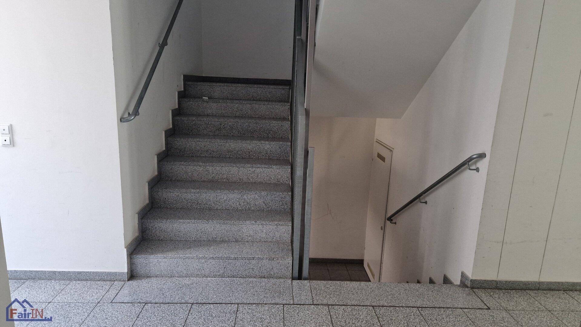 Geräumiges Treppenhaus mit robusten Steinfliesen und Metallgeländer, das die Stockwerke verbindet.