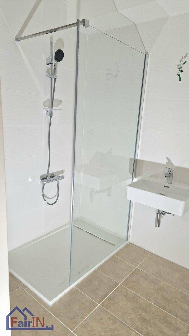 Modernes Badezimmer mit ebenerdiger Glasdusche und einem einzelnen Waschbecken, hell gefliest.