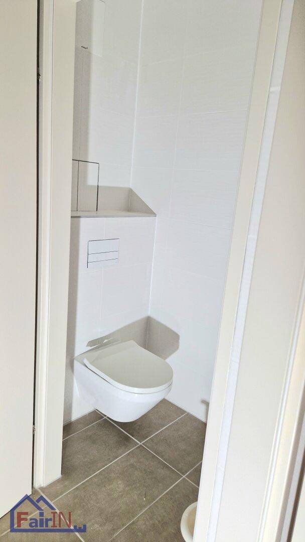 Separates WC mit wandhängender Toilette und modernen Fliesen, ideal für Gäste.