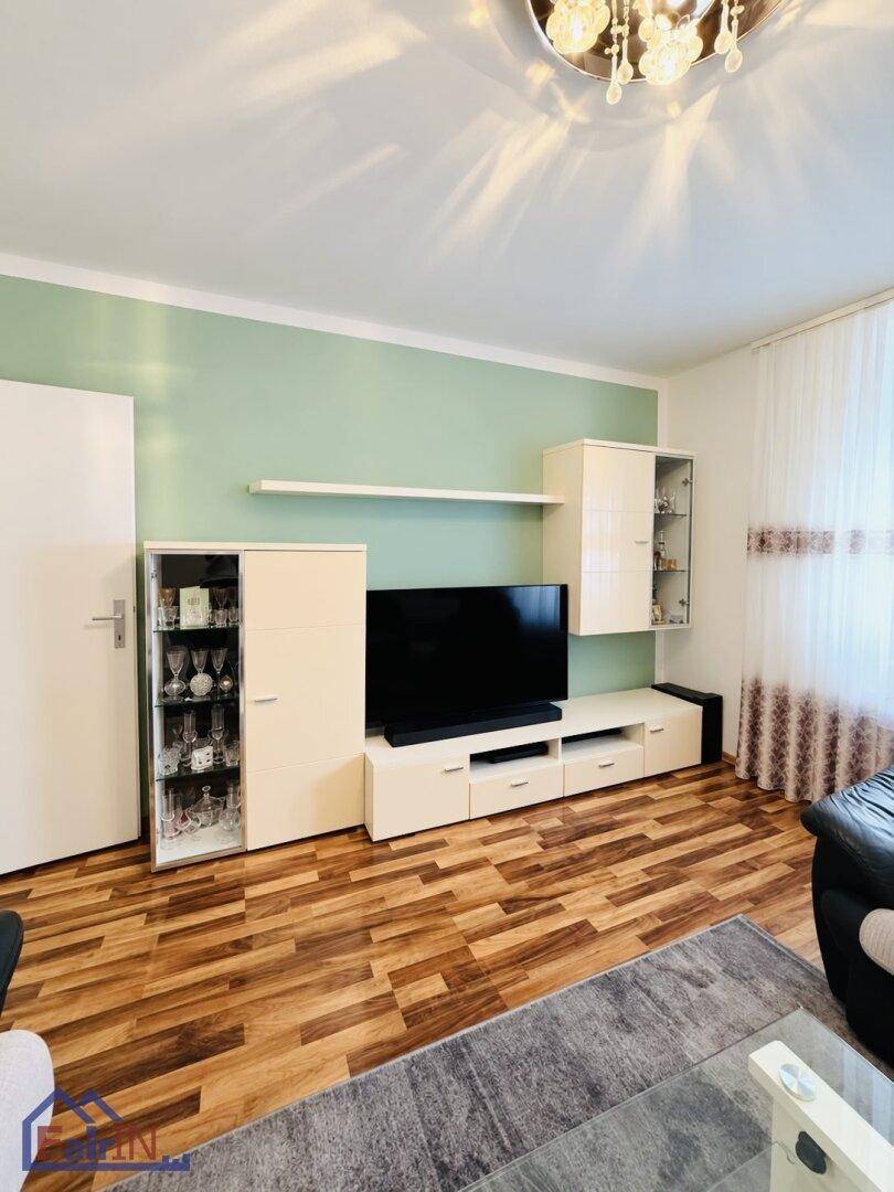 Helles Wohnzimmer mit modernem TV-Möbel, Laminatboden und einer hellgrünen Akzentwand.