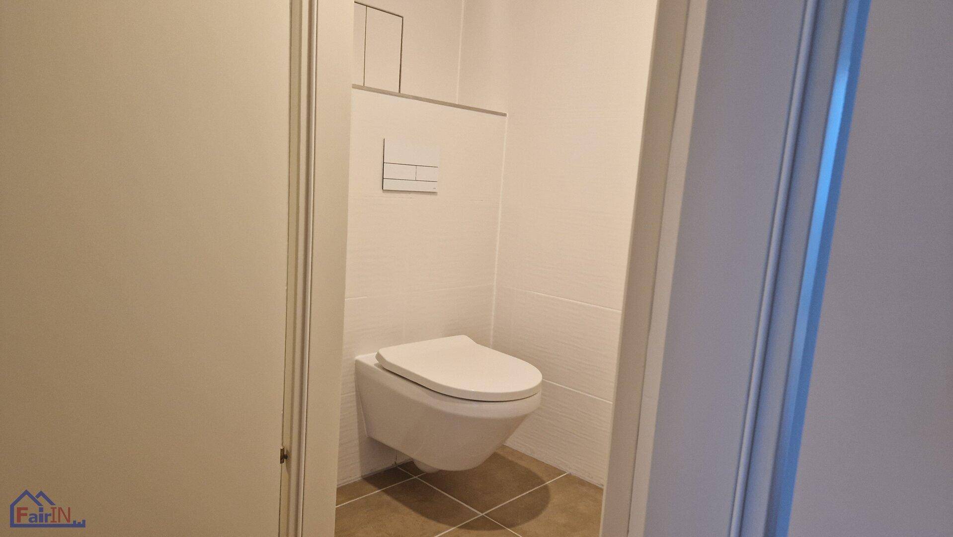 Separates WC mit wandhängender Toilette und modernen weißen Fliesen.