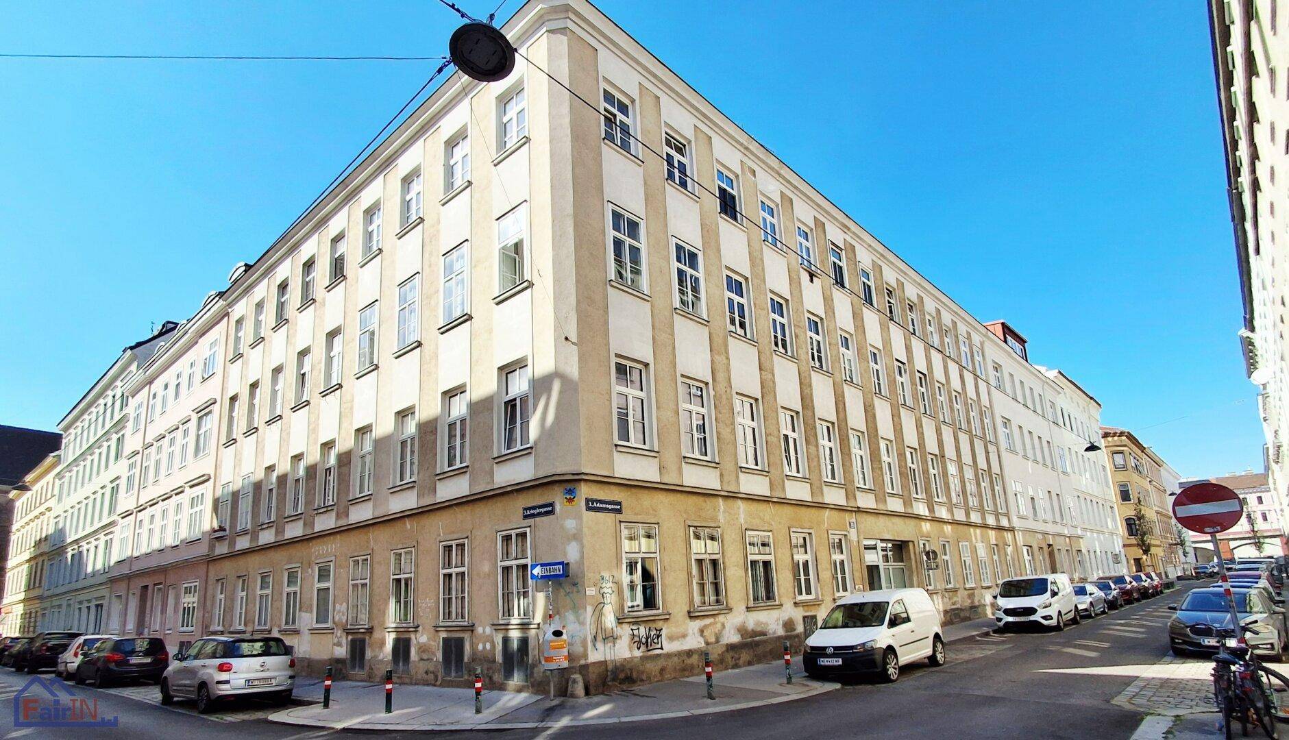Historisches Eckgebäude in der Stadt mit vielen Fenstern und geparkten Fahrzeugen.