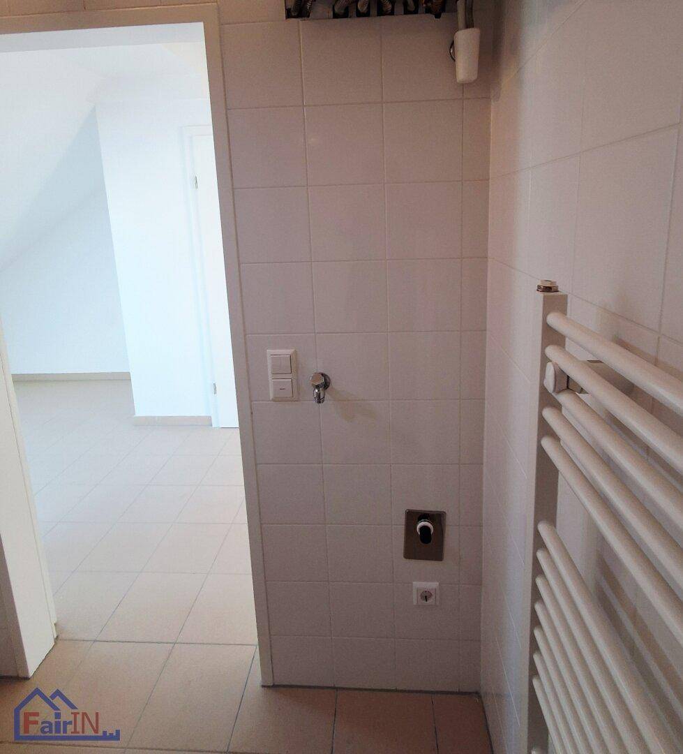 Gefliester Badezimmerbereich mit Handtuchheizkörper und Anschluss für eine Waschmaschine.