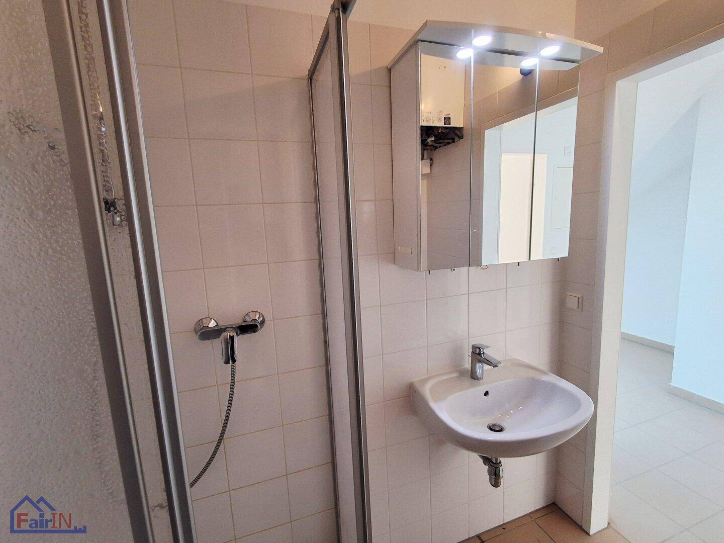 Badezimmer mit Duschkabine, Waschbecken und Spiegelschrank über dem Waschtisch.