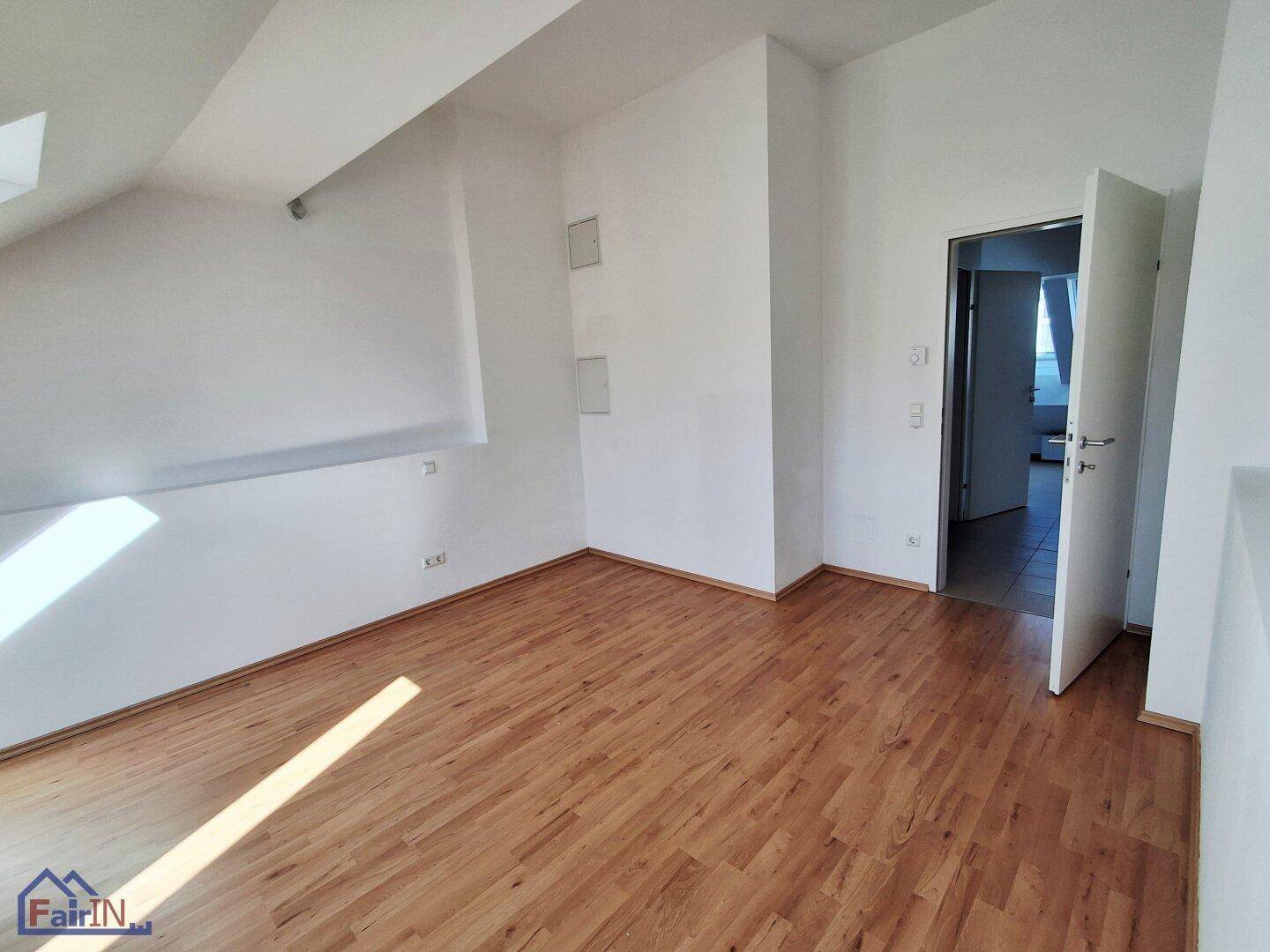 Heller Wohnraum im Dachgeschoss mit Holzfußboden und schrägen Wänden.