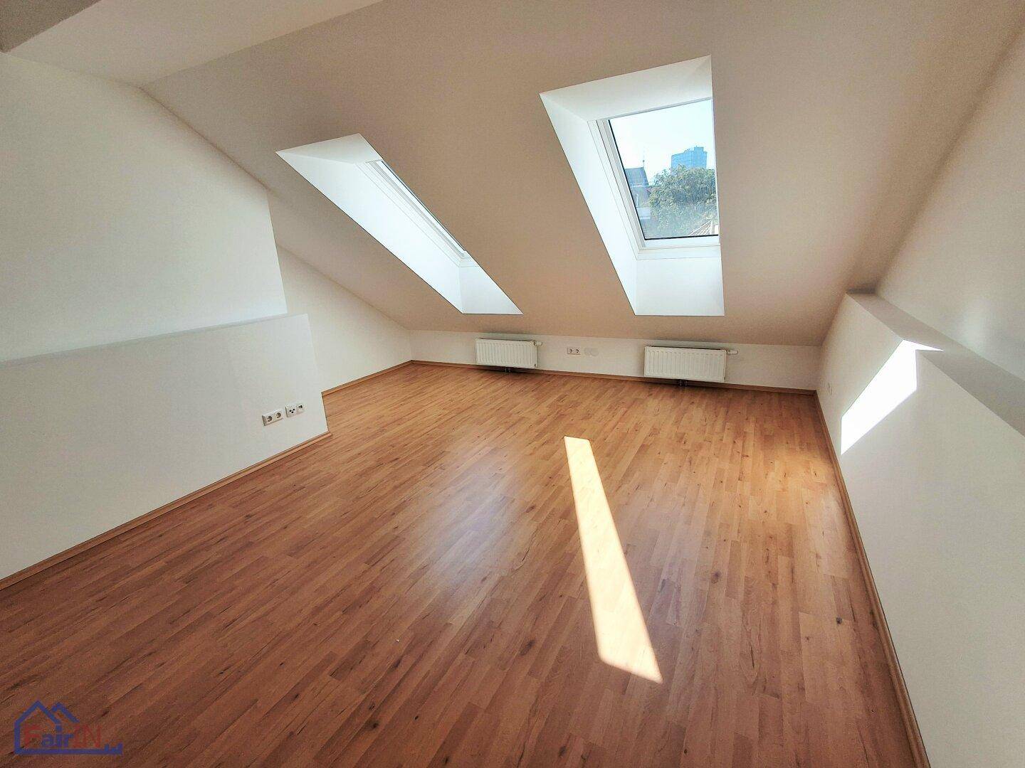 Geräumiger Wohnraum im Dachgeschoss mit Holzboden und zwei großen Dachfenstern.