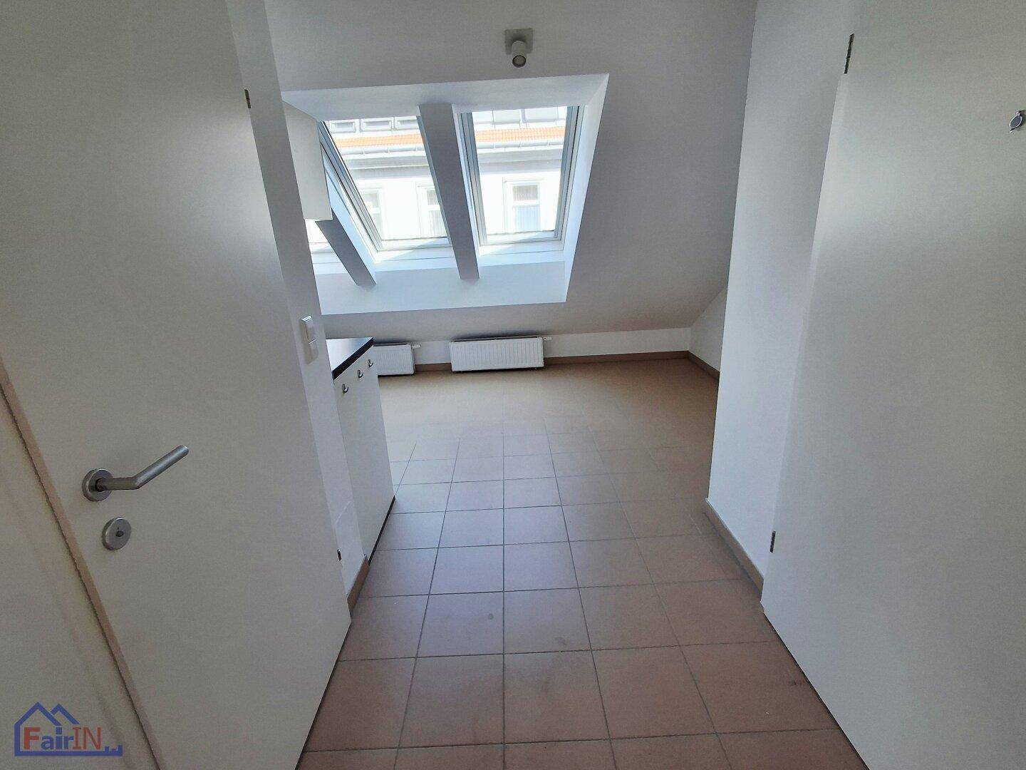 Eingangsbereich mit Fliesenboden, der zu einem hellen Raum mit Dachfenstern führt.