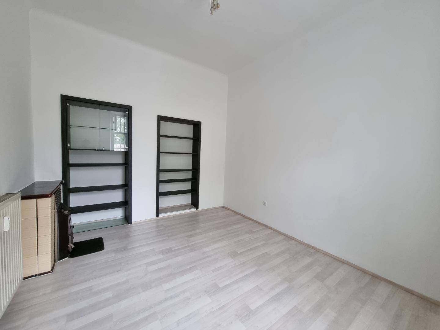 Heller Raum mit hellem Laminatboden, weißen Wänden und zwei integrierten Regalen für Stauraum.