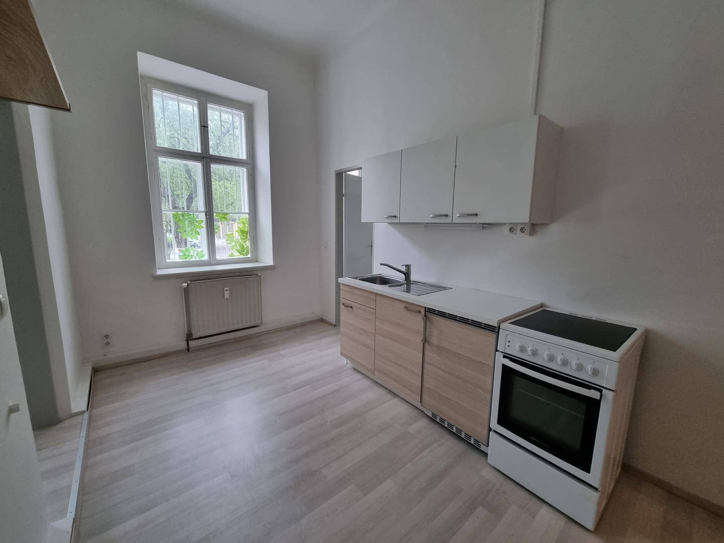 Kompakte Küche mit hellen Holzschränken, Herd und Spüle, gut beleuchtet durch ein Fenster.