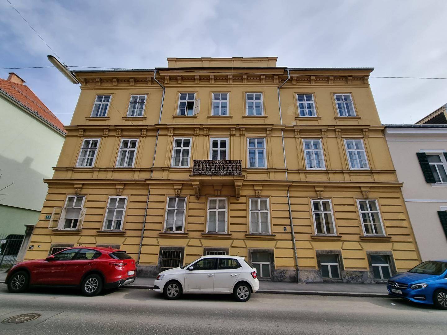 Historisches Mehrfamilienhaus mit gelber Fassade und vielen Fenstern an einer städtischen Straße.