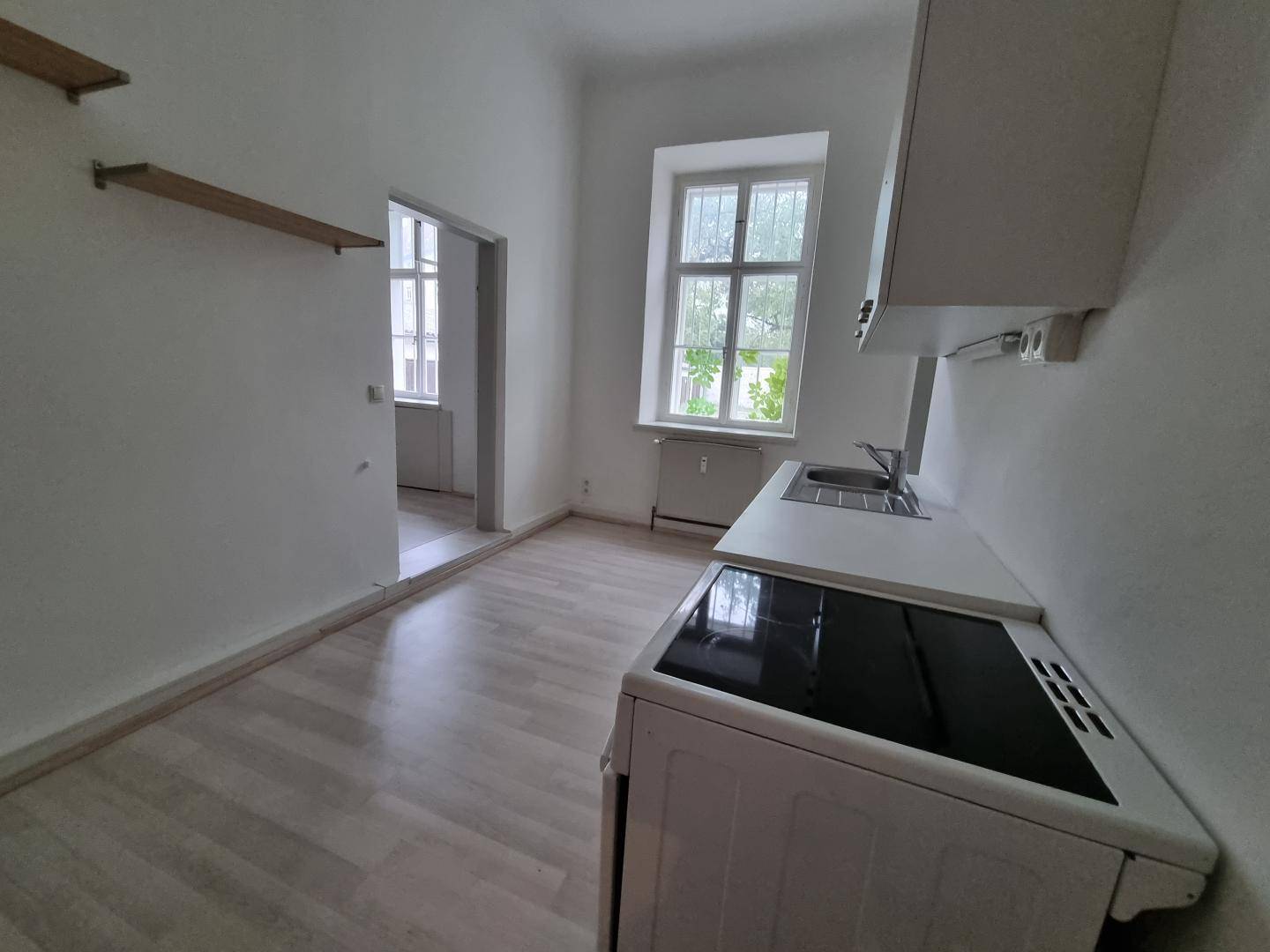 Kleine Küche mit Herd, Spüle und Arbeitsfläche, hellen Wänden und Laminatboden, mit Fenster.