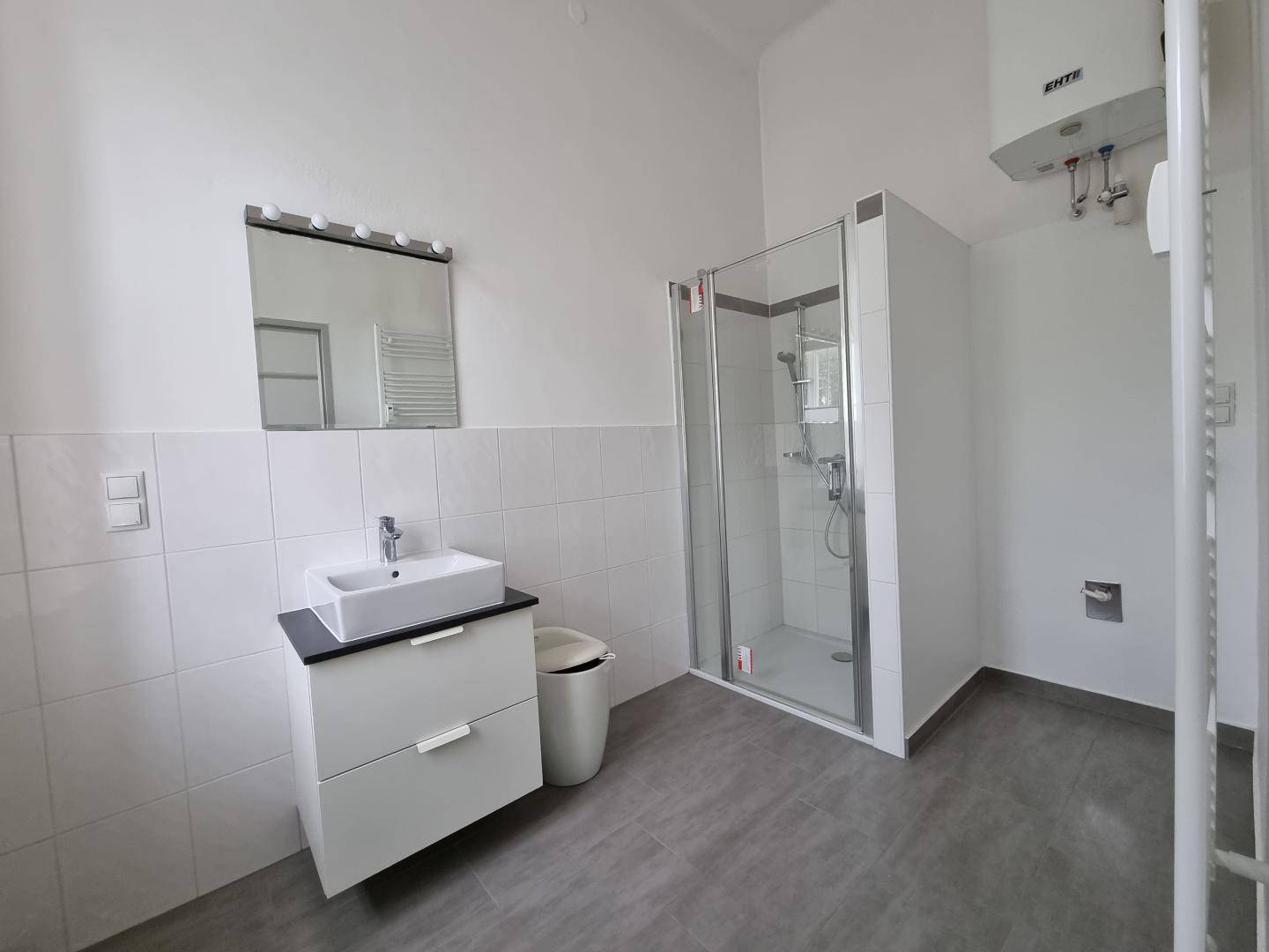 Modernes Badezimmer mit Duschkabine, Waschbecken und hellgrauen Fliesen, inklusive Warmwasserboiler.