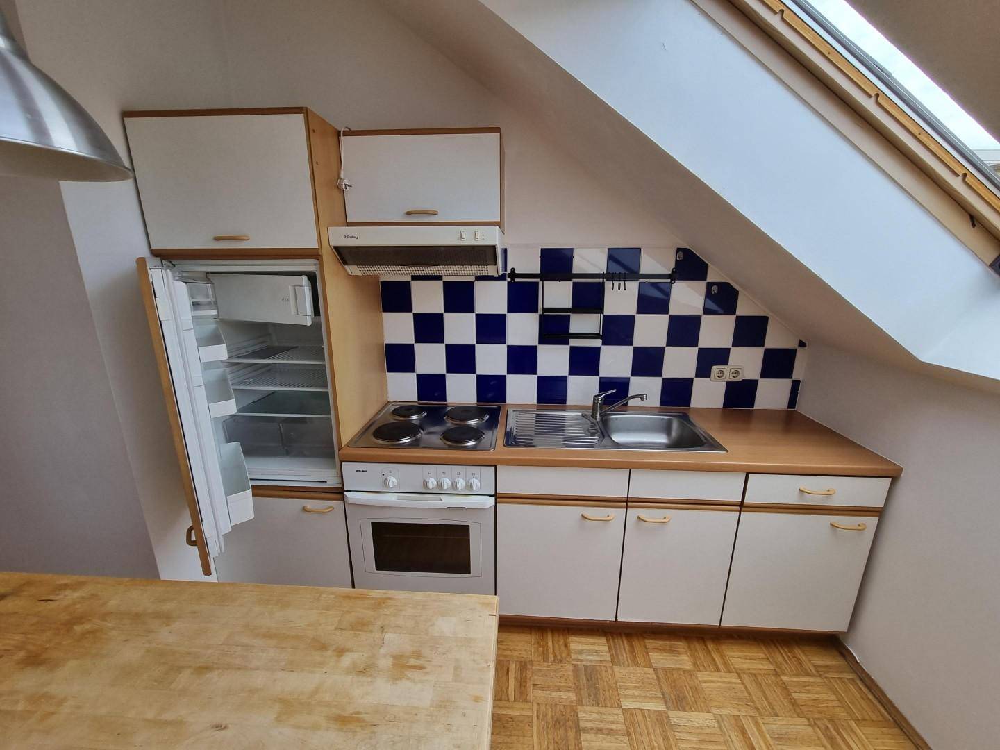 Funktionale Küchenzeile im Dachgeschoss mit Herd, Spüle und Kühlschrank unter Dachschrägen.