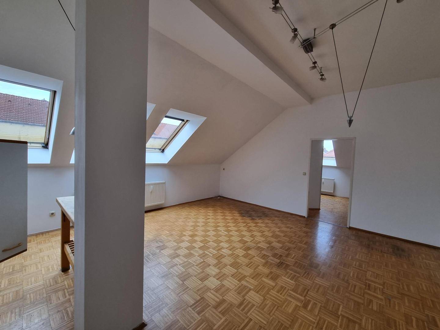 Heller Wohnbereich im Dachgeschoss mit Parkettboden und Zugang zu weiteren Räumen.