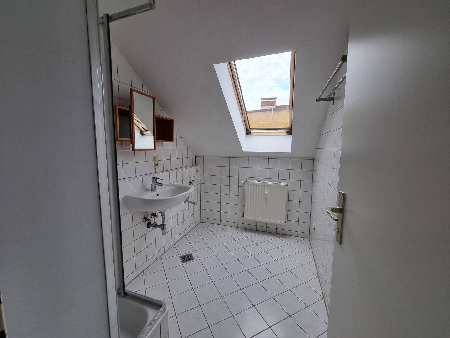 Helles Badezimmer im Dachgeschoss mit Dusche, Waschbecken und Dachfenster.