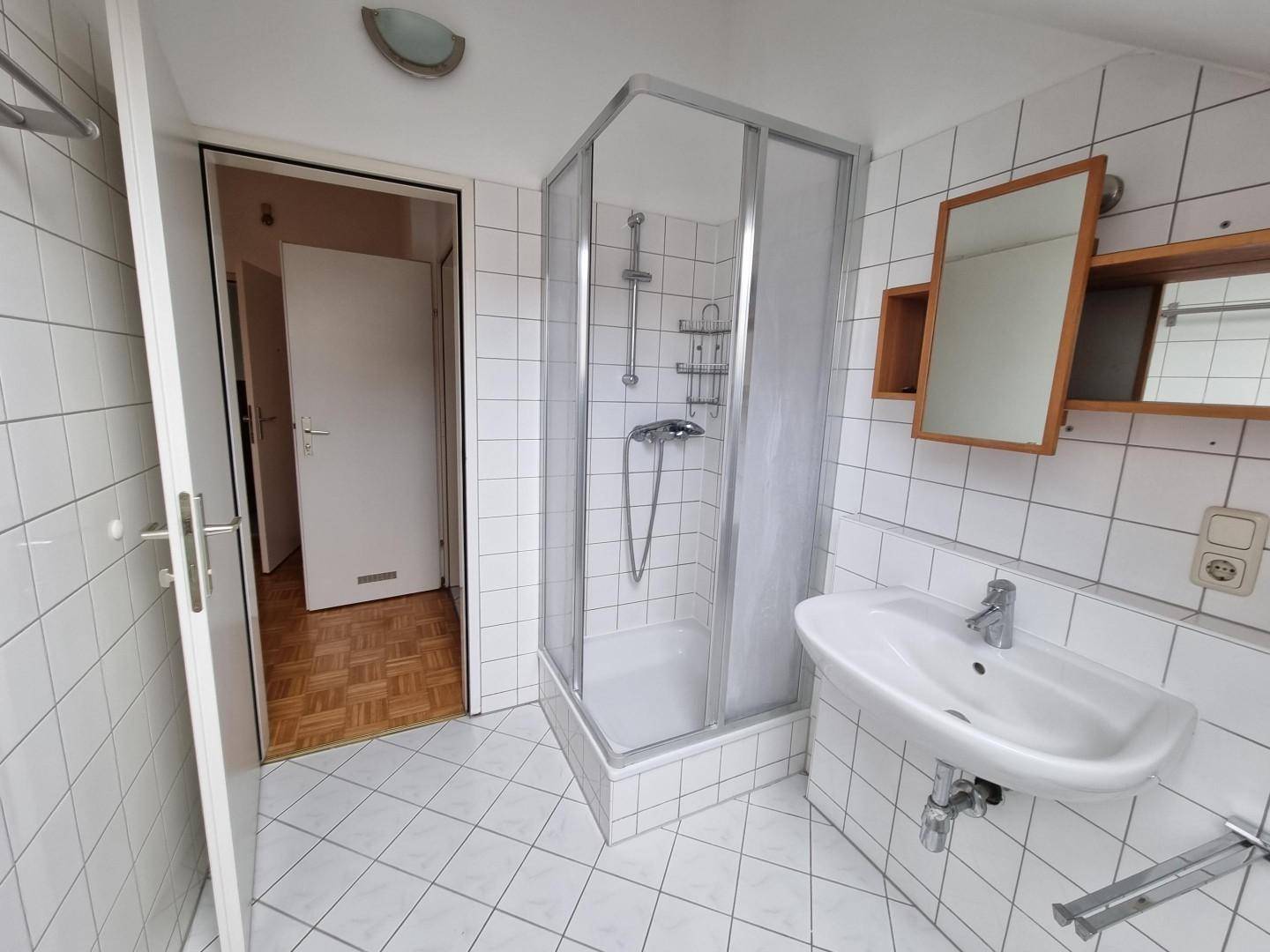 Badezimmer mit Duschkabine, Waschbecken und weiß gefliesten Wänden.