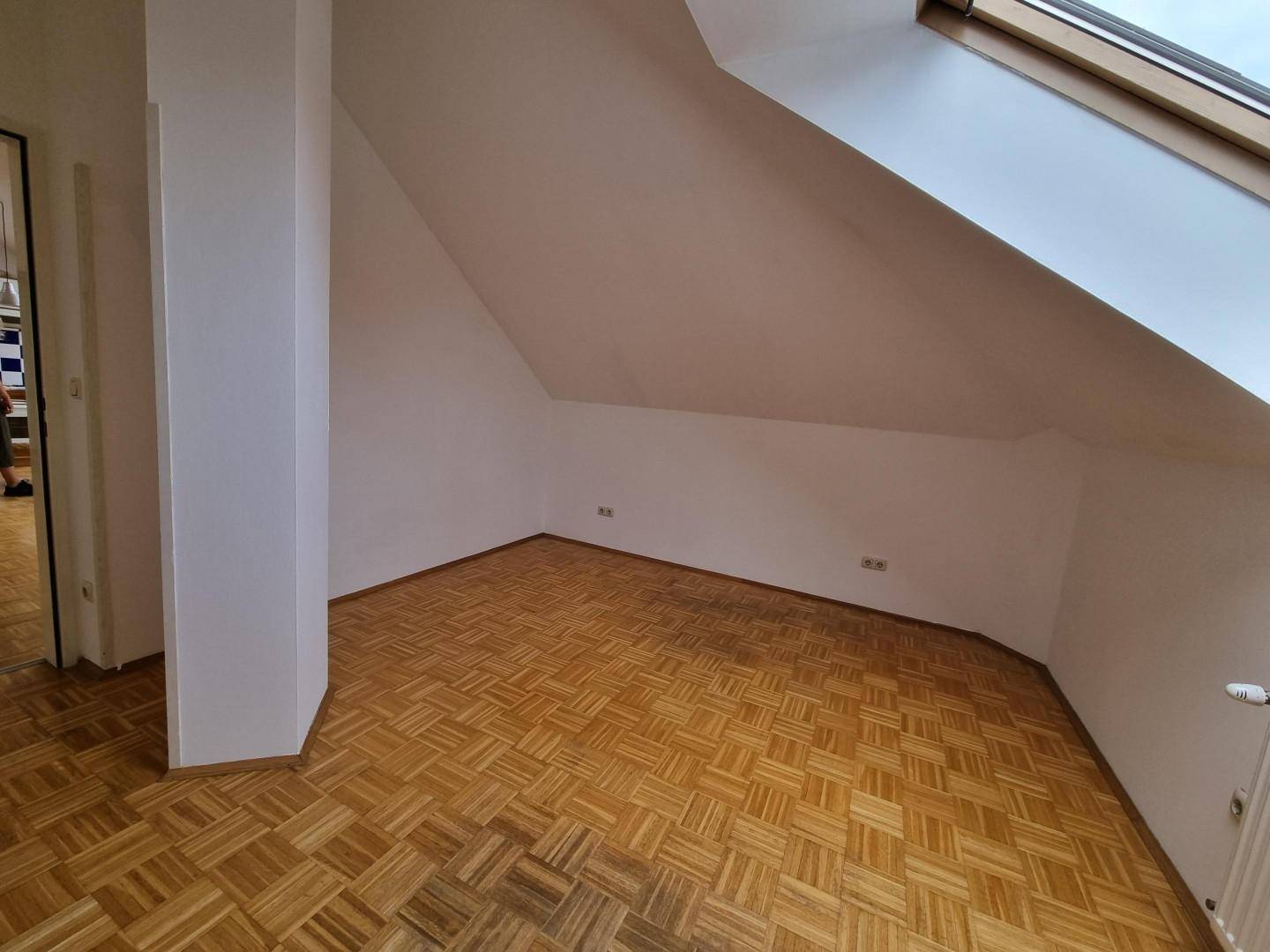 Leeres Zimmer im Dachgeschoss mit Parkettboden und schrägen Wänden, bereit zur Einrichtung.