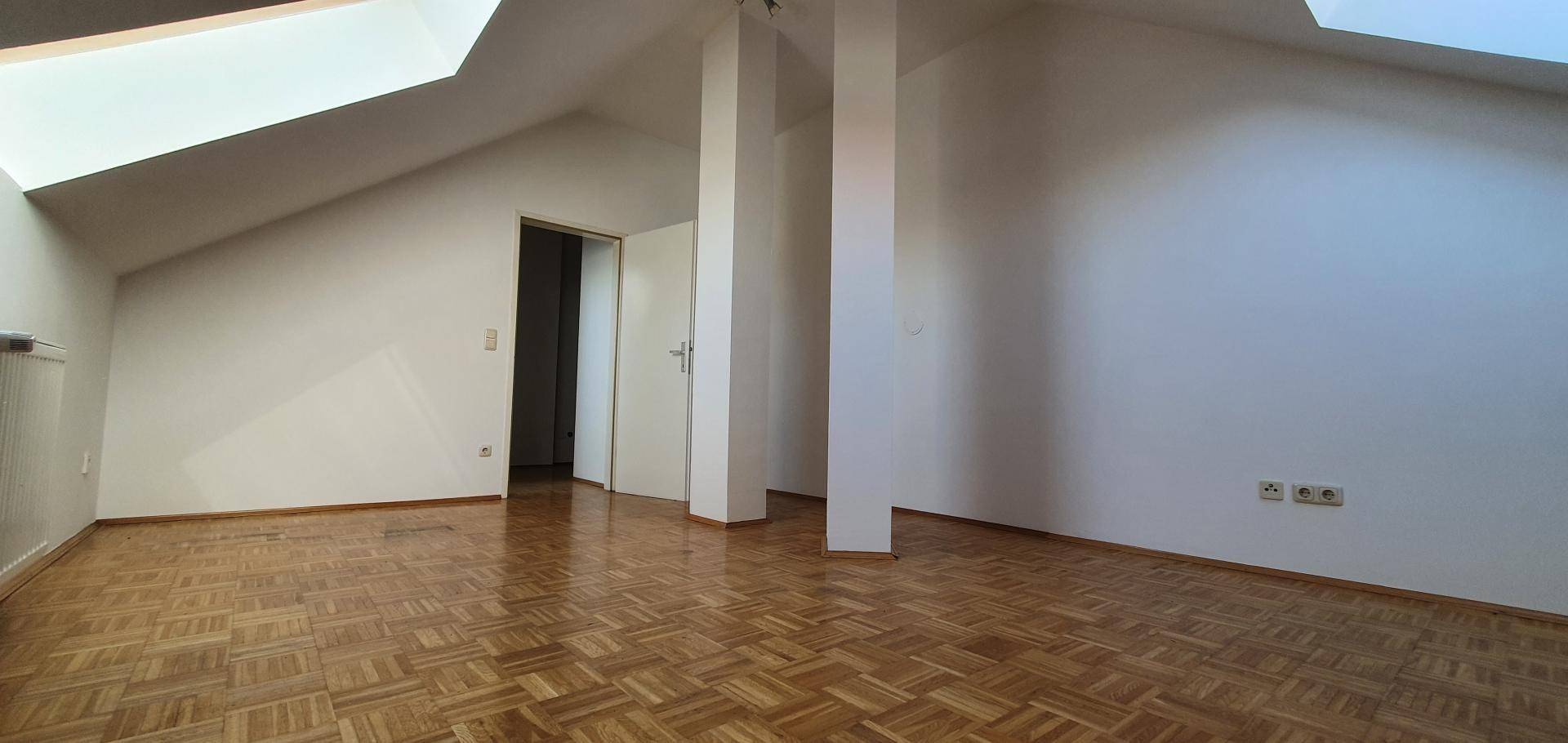 Geräumiger Wohnbereich im Dachgeschoss mit Parkettboden und viel Tageslicht durch Dachfenster.