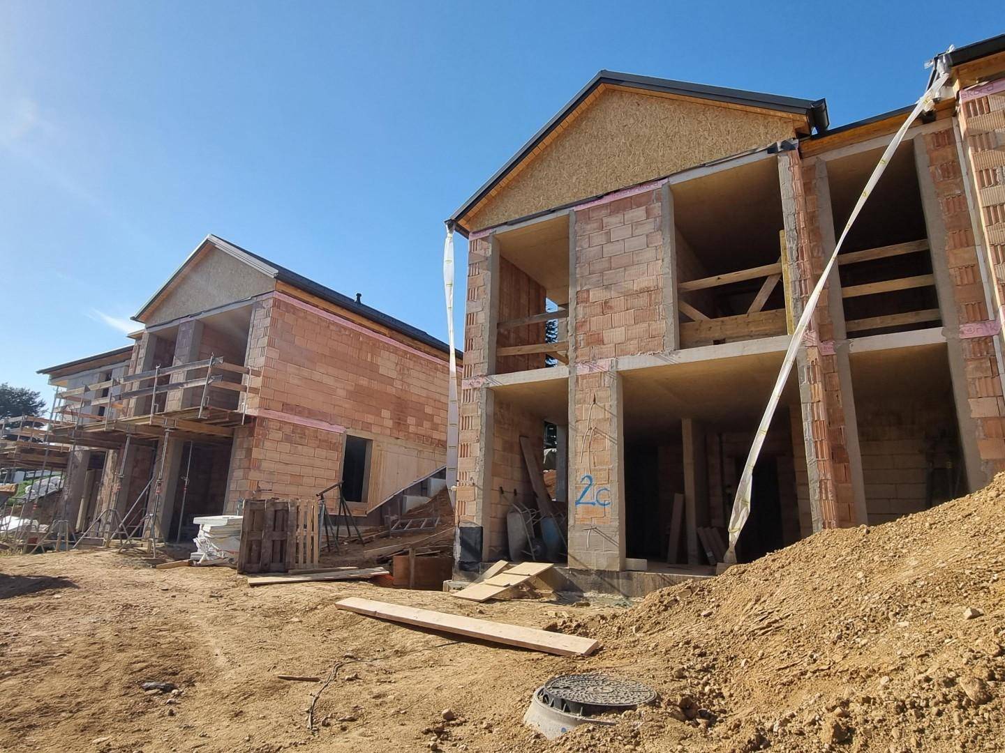 Reihenhäuser im Rohbau auf einer sonnigen Baustelle mit Ziegelwänden und Holzkonstruktionen.