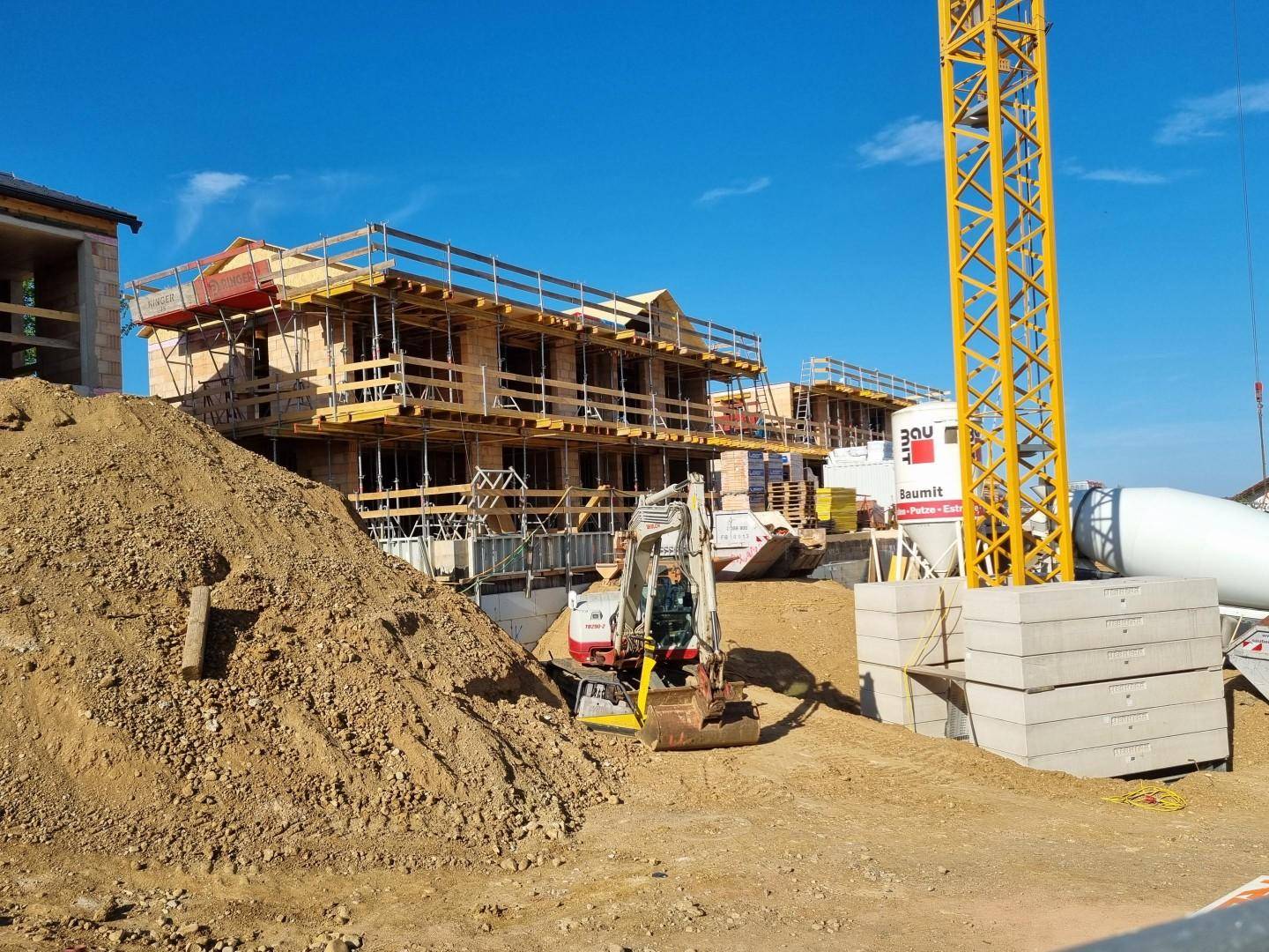 Baustelle mit im Bau befindlichen Gebäuden, einem Kran und Erdhügeln.
