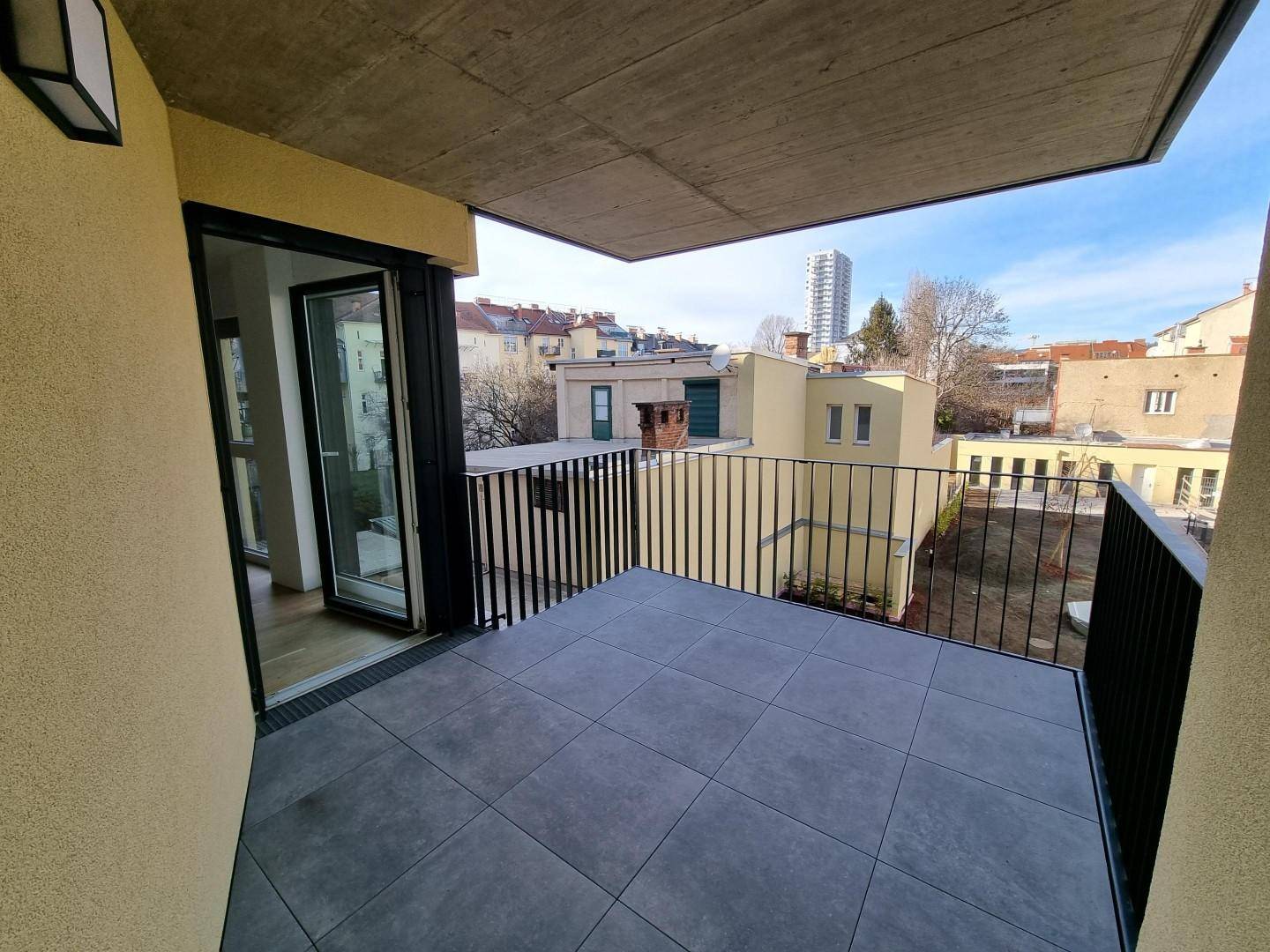 Geräumiger Balkon mit Fliesenboden und Blick auf die Stadt und umliegende Gebäude.