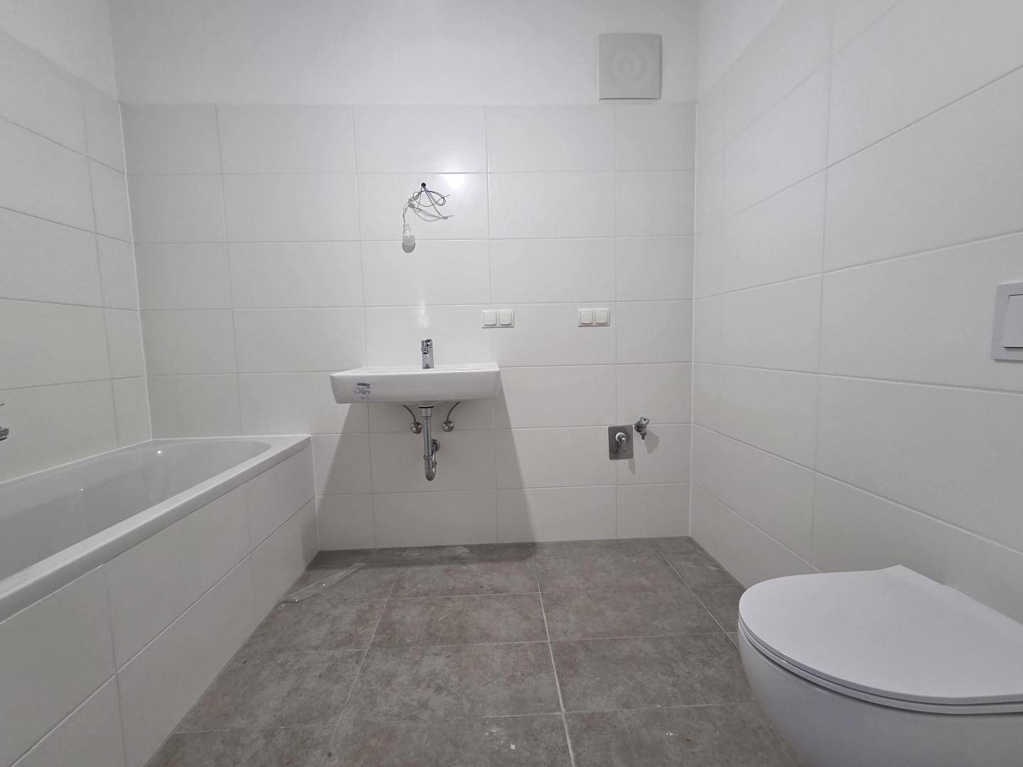 Modernes Badezimmer mit weißen Fliesen, Badewanne, Waschbecken und Toilette in neuwertigem Zustand.