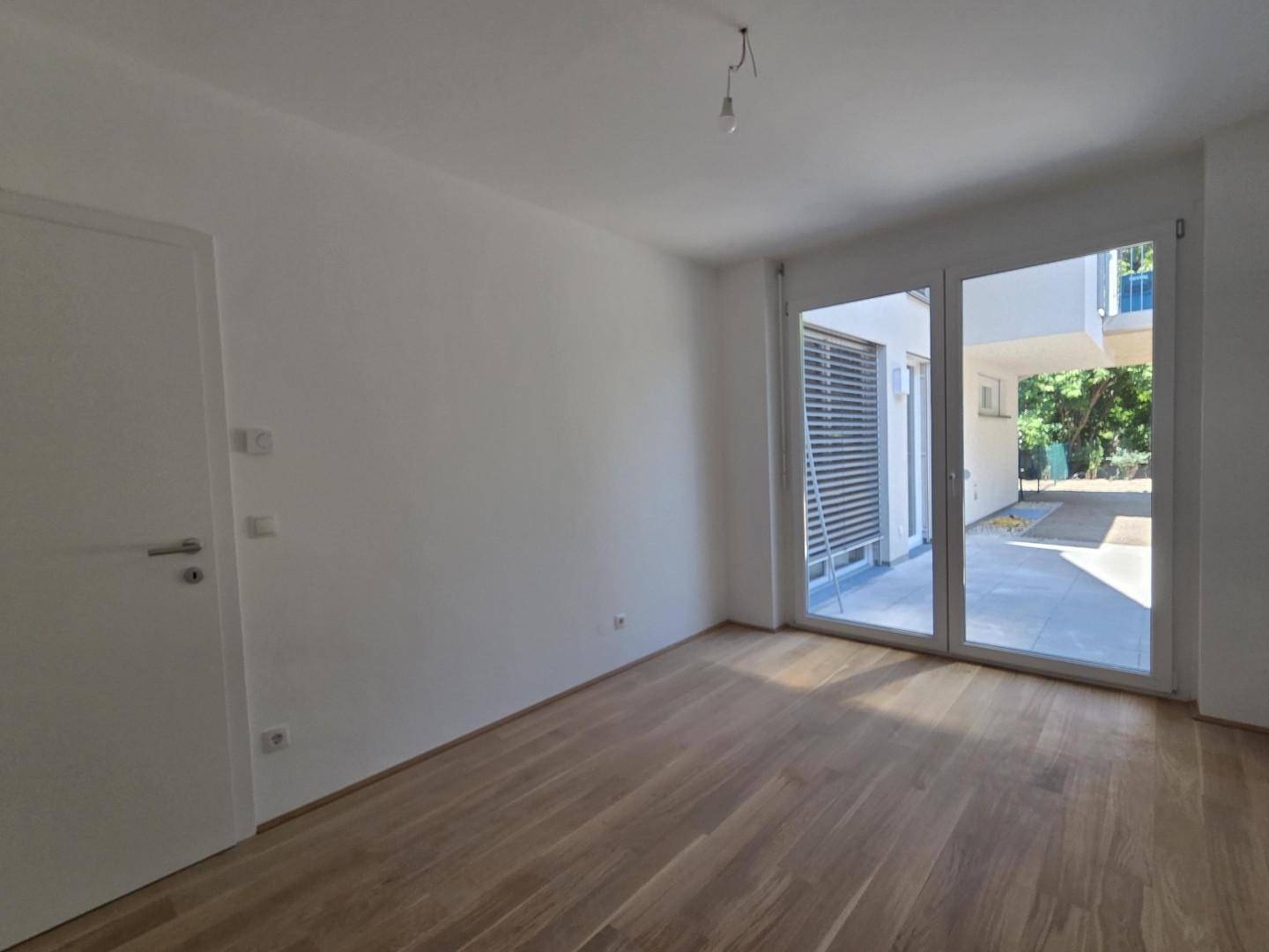 Heller Raum mit Parkettboden und Zugang zu einem Außenbereich, ideal als Schlafzimmer.