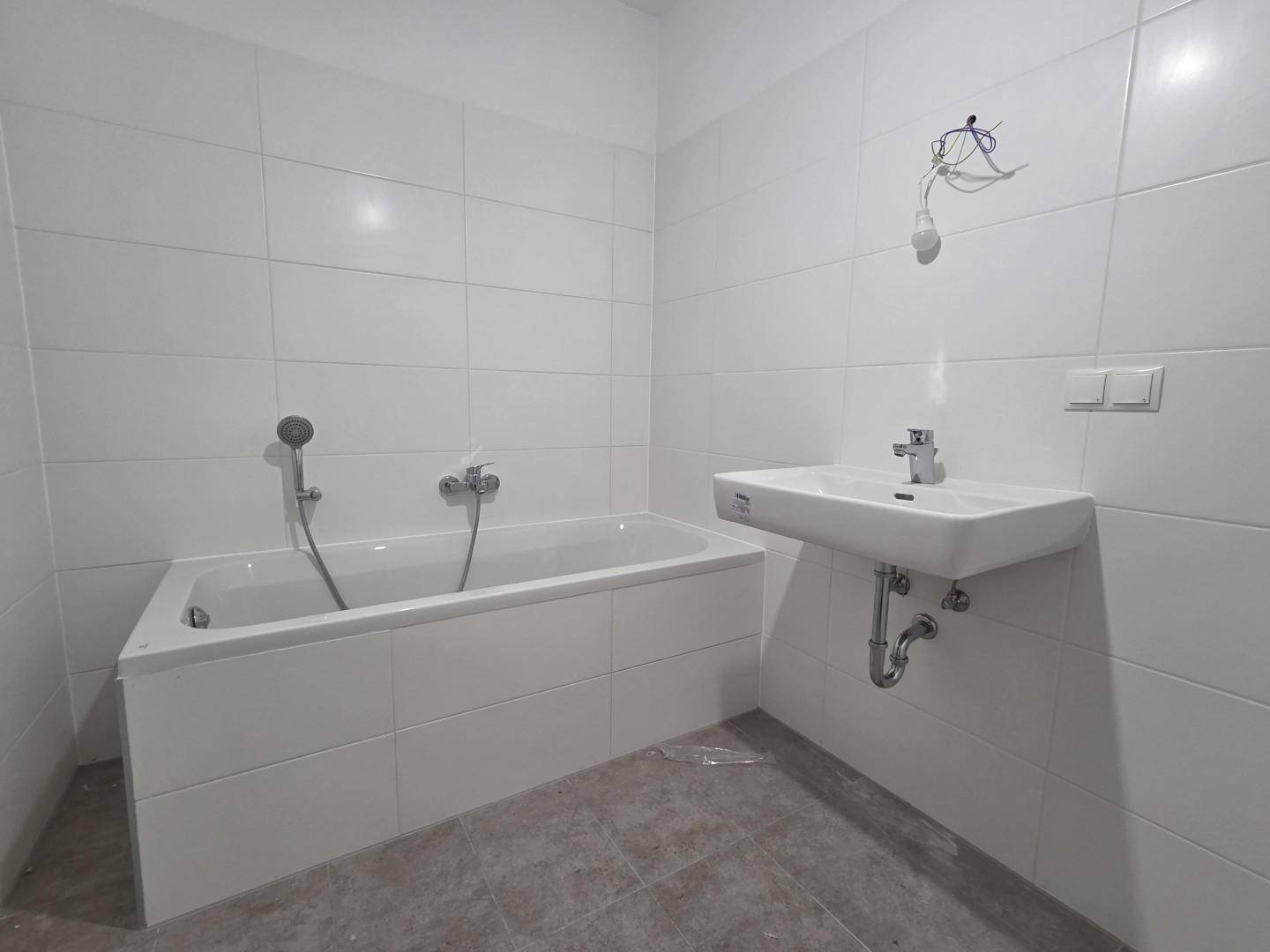 Sauberes Badezimmer mit Badewanne, Waschbecken und weißen Wandfliesen in neuwertigem Zustand.