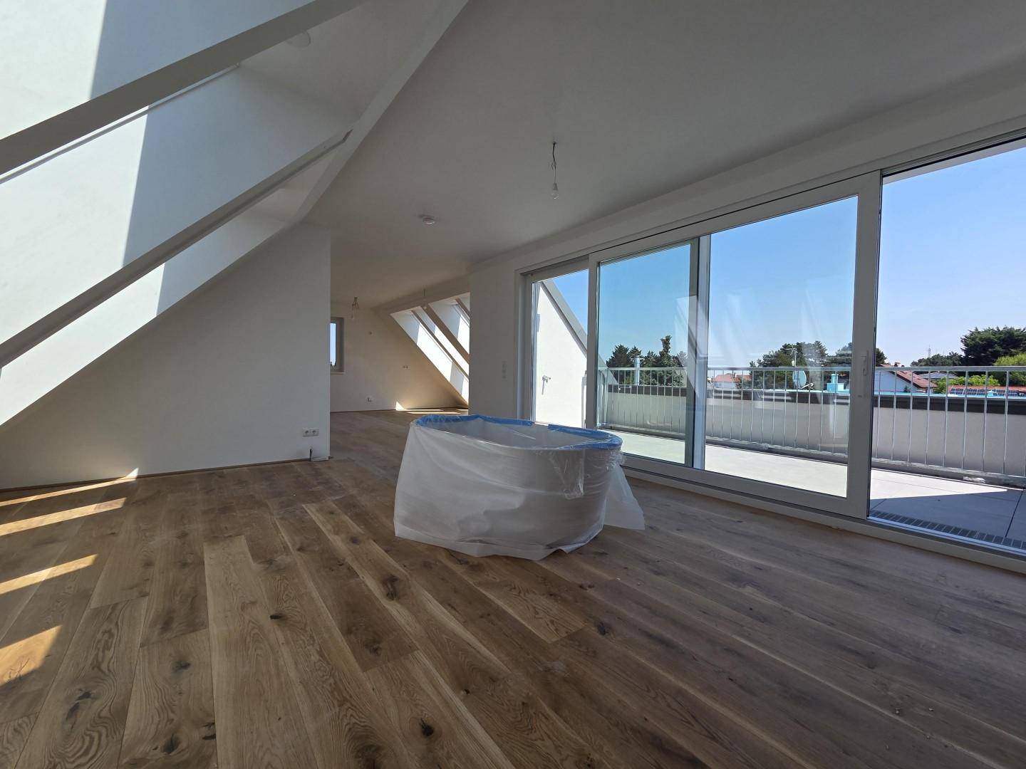 Heller Raum im Dachgeschoss mit Holzboden und Zugang zu einer großen Außenterrasse.