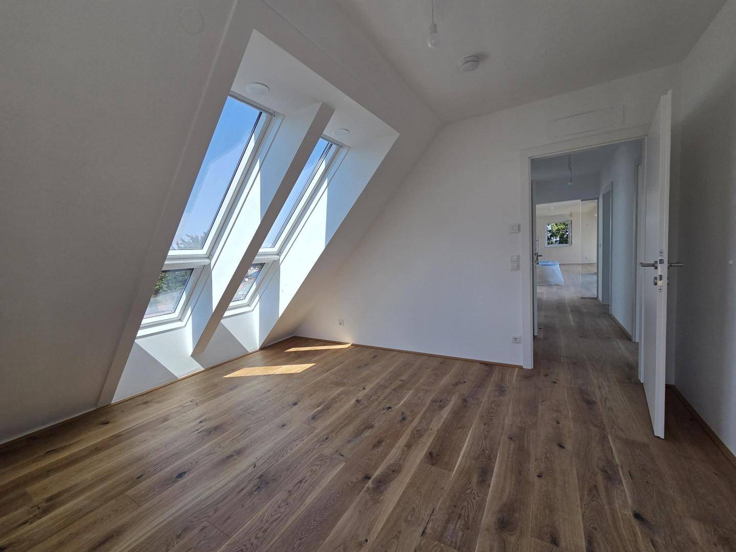Heller Flur im Dachgeschoss mit Holzboden und Dachfenstern, der zu weiteren Räumen führt.