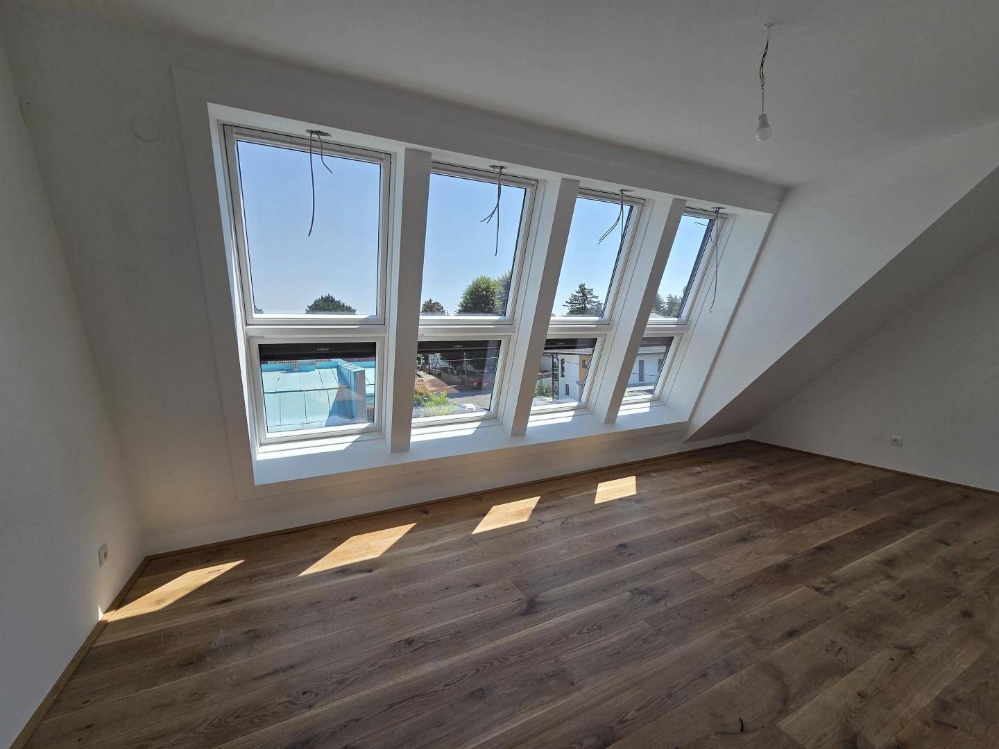 Geräumiges Dachgeschosszimmer mit Holzboden und einer Reihe von Dachfenstern, die viel Licht spenden.