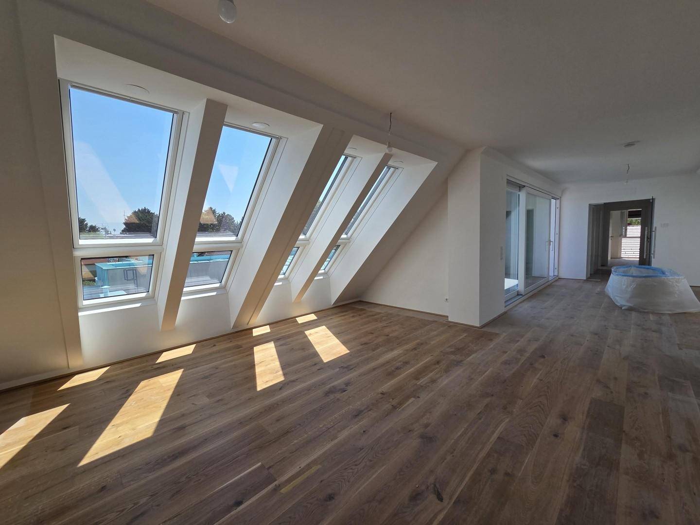 Geräumiges Dachgeschosszimmer mit Holzboden und großen Fenstern, die zu einer Terrasse führen.